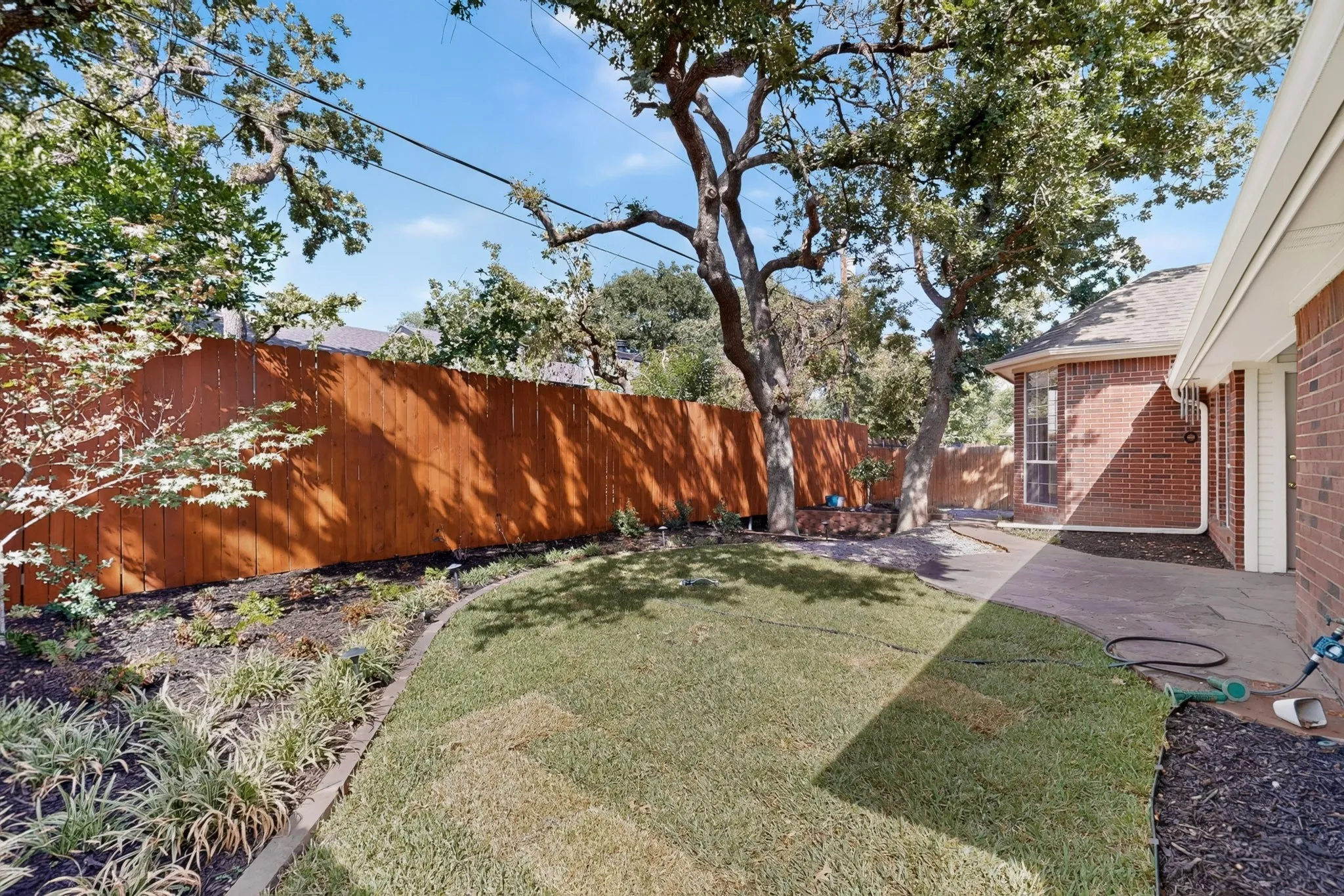 Private backyard featuring a wood privacy fence, mature trees, manicured lawn, and a paved patio area
