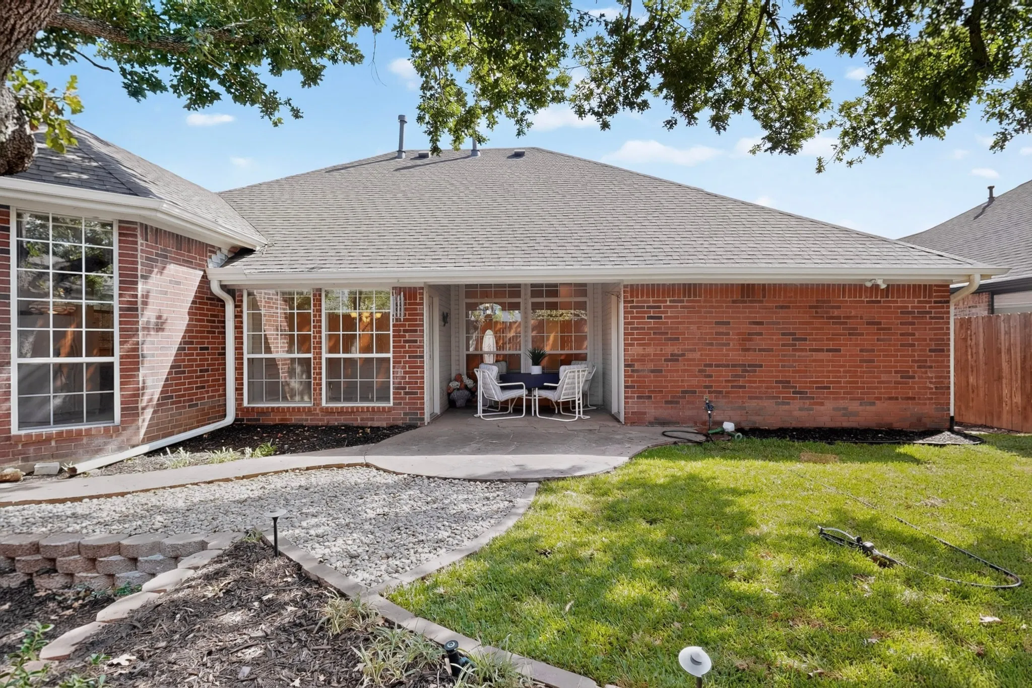 Brick exterior with an extended covered patio, multiple large windows, and a landscaped gravel path