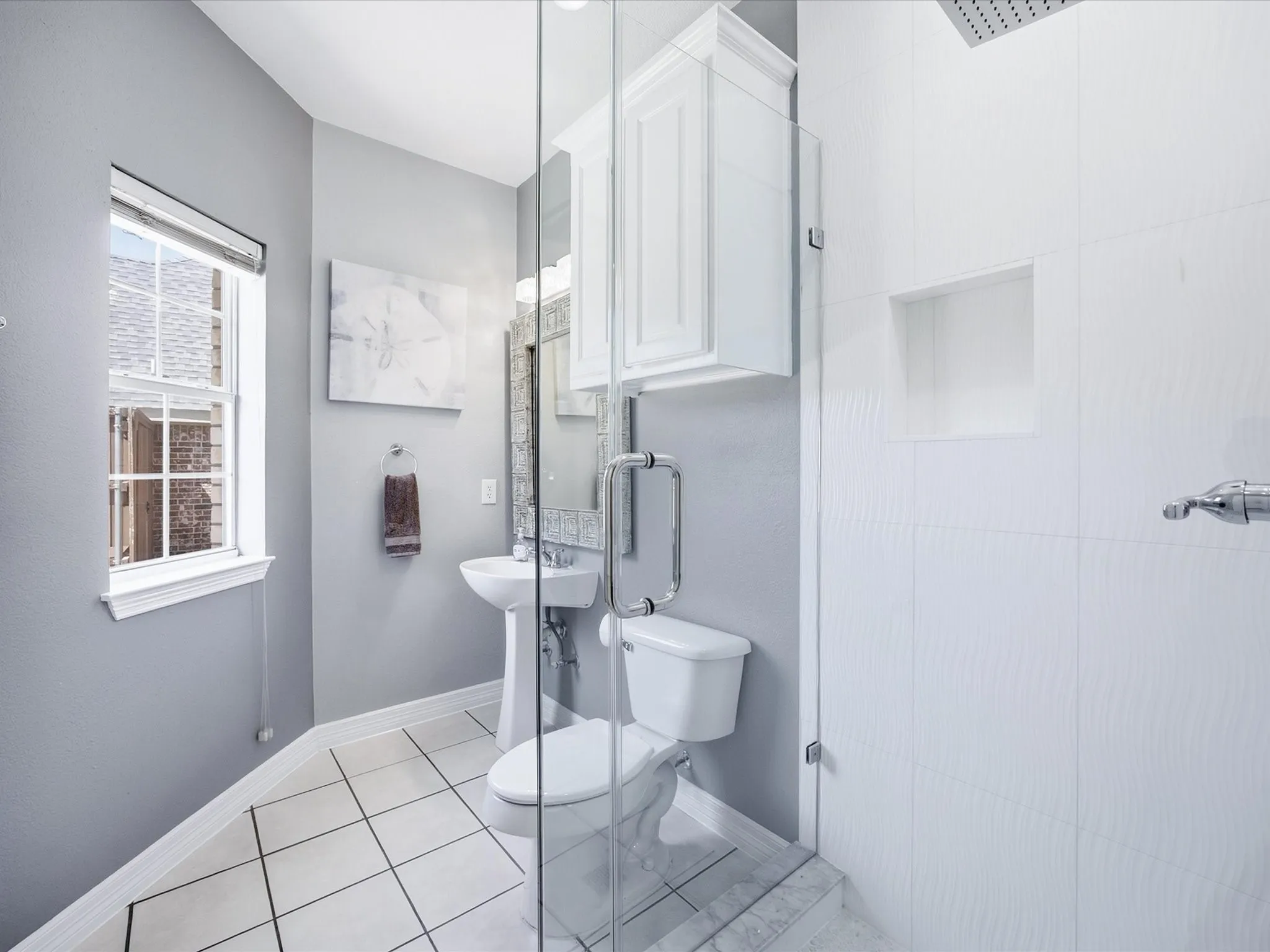 Pedestal sink, wall-mounted cabinetry, glass-enclosed shower, rain shower head, and recessed shower niche