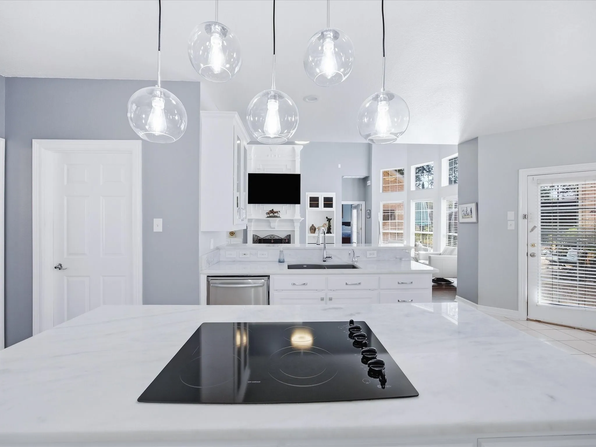 White kitchen island with an integrated black electric cooktop, white perimeter cabinetry, and marble-finish countertops