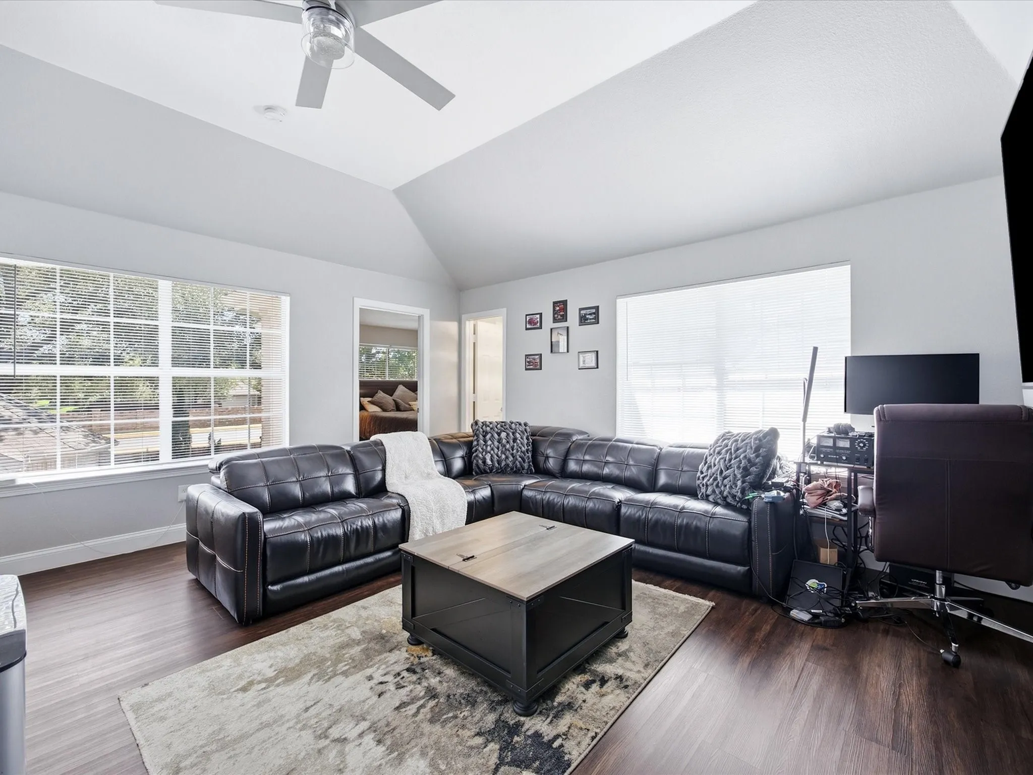 Vaulted ceiling with a ceiling fan, wood-finish flooring, and multiple windows