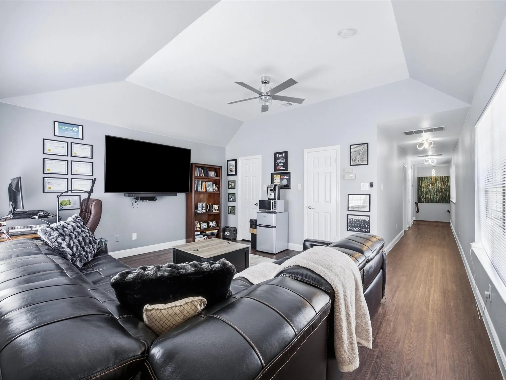 Vaulted ceiling with a ceiling fan, wall-mounted television, built-in shelving, wood-finish flooring, and white interior doors