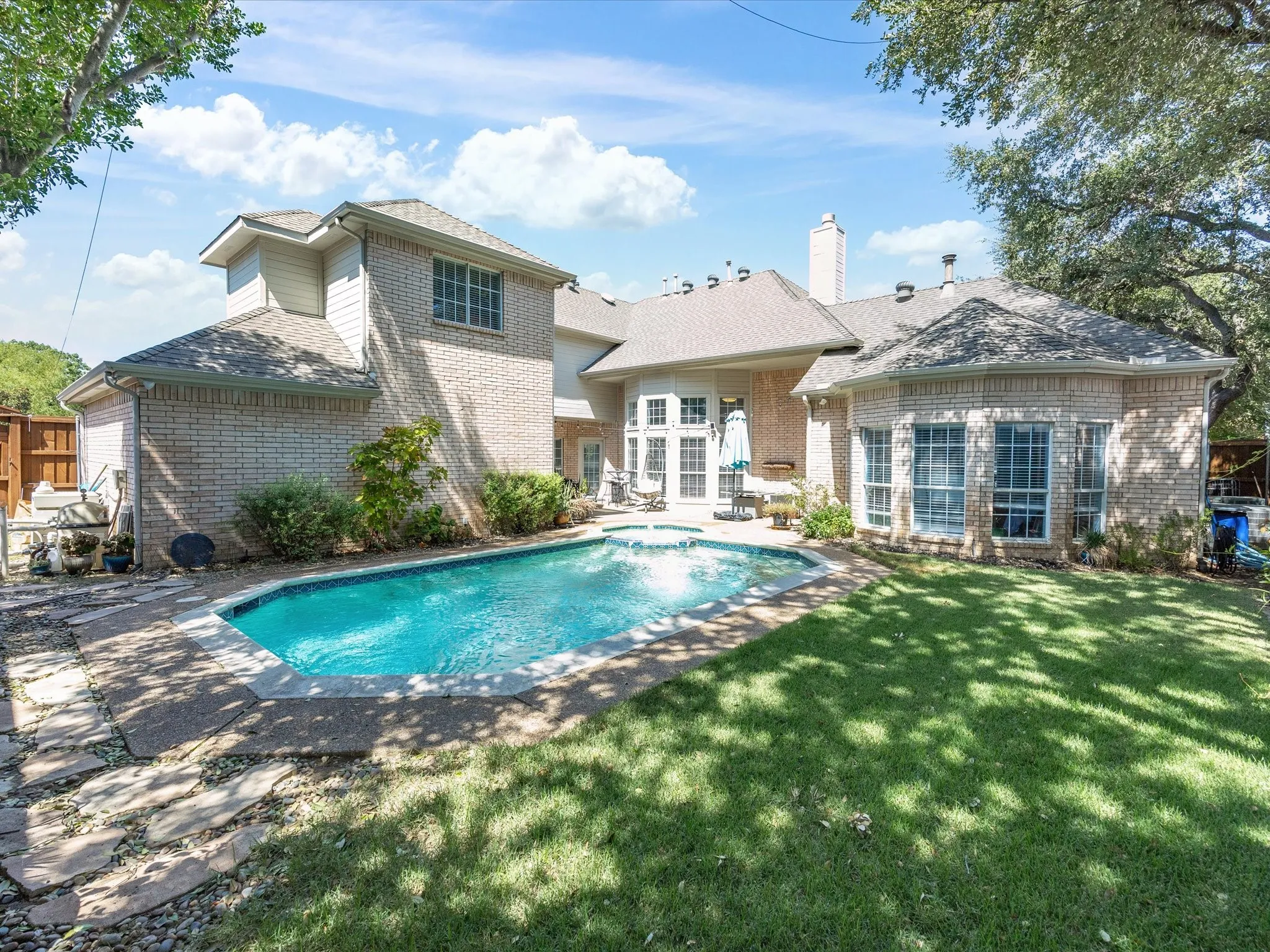 Expansive backyard featuring a blue swimming pool with flagstone coping, a lush lawn, and a brick exterior