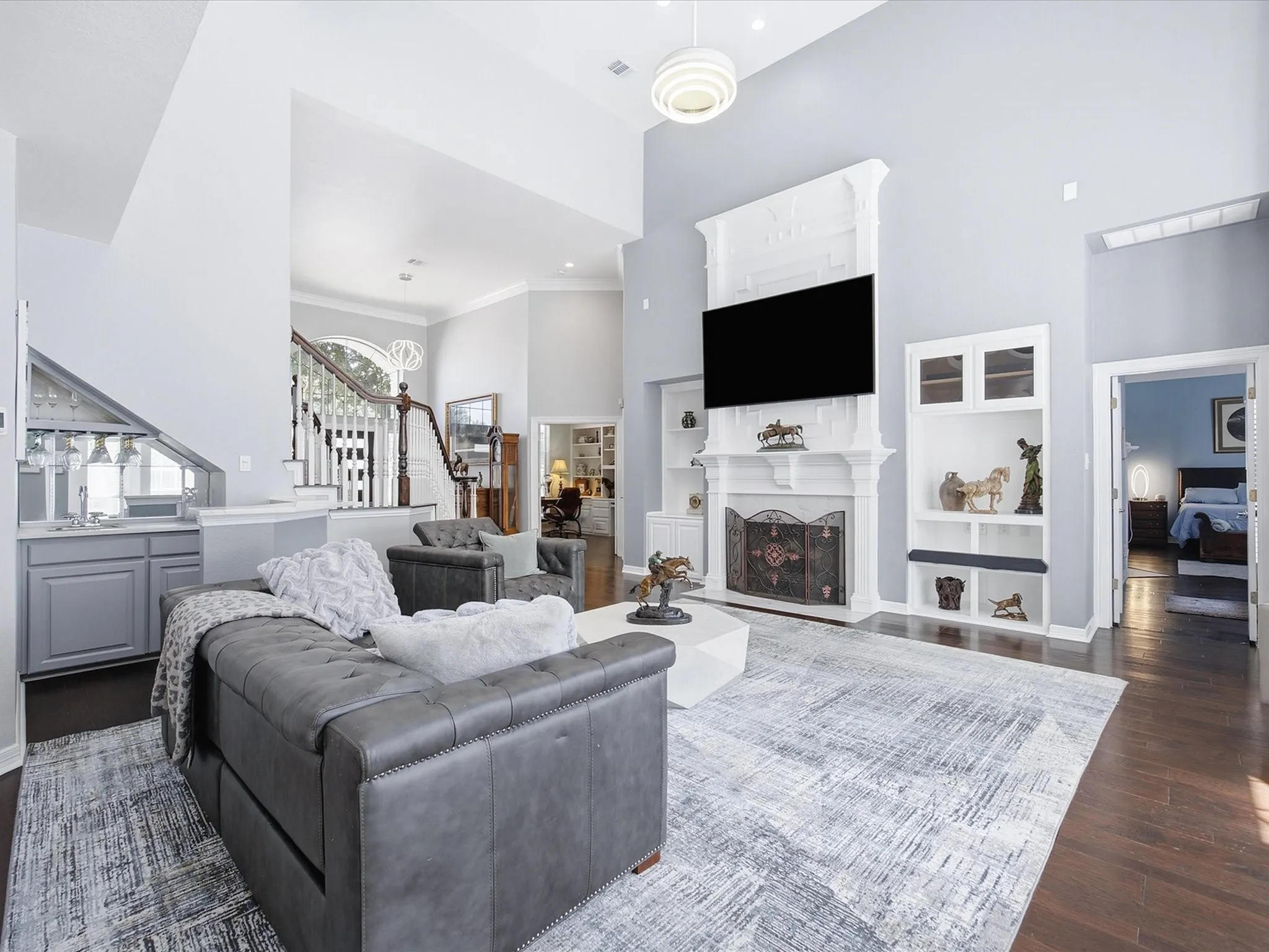 Two-story living area featuring dark wood-finish flooring, a built-in wet bar, and a fireplace with an ornate mantel