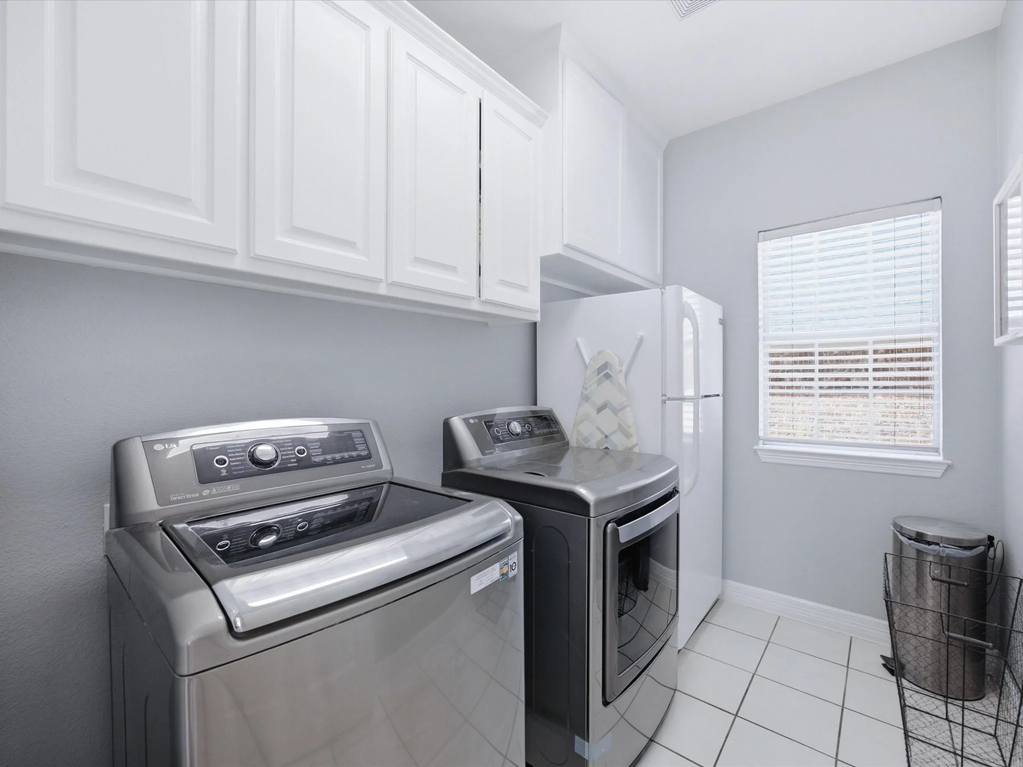 White upper cabinetry, white tile flooring, and a single window with blinds