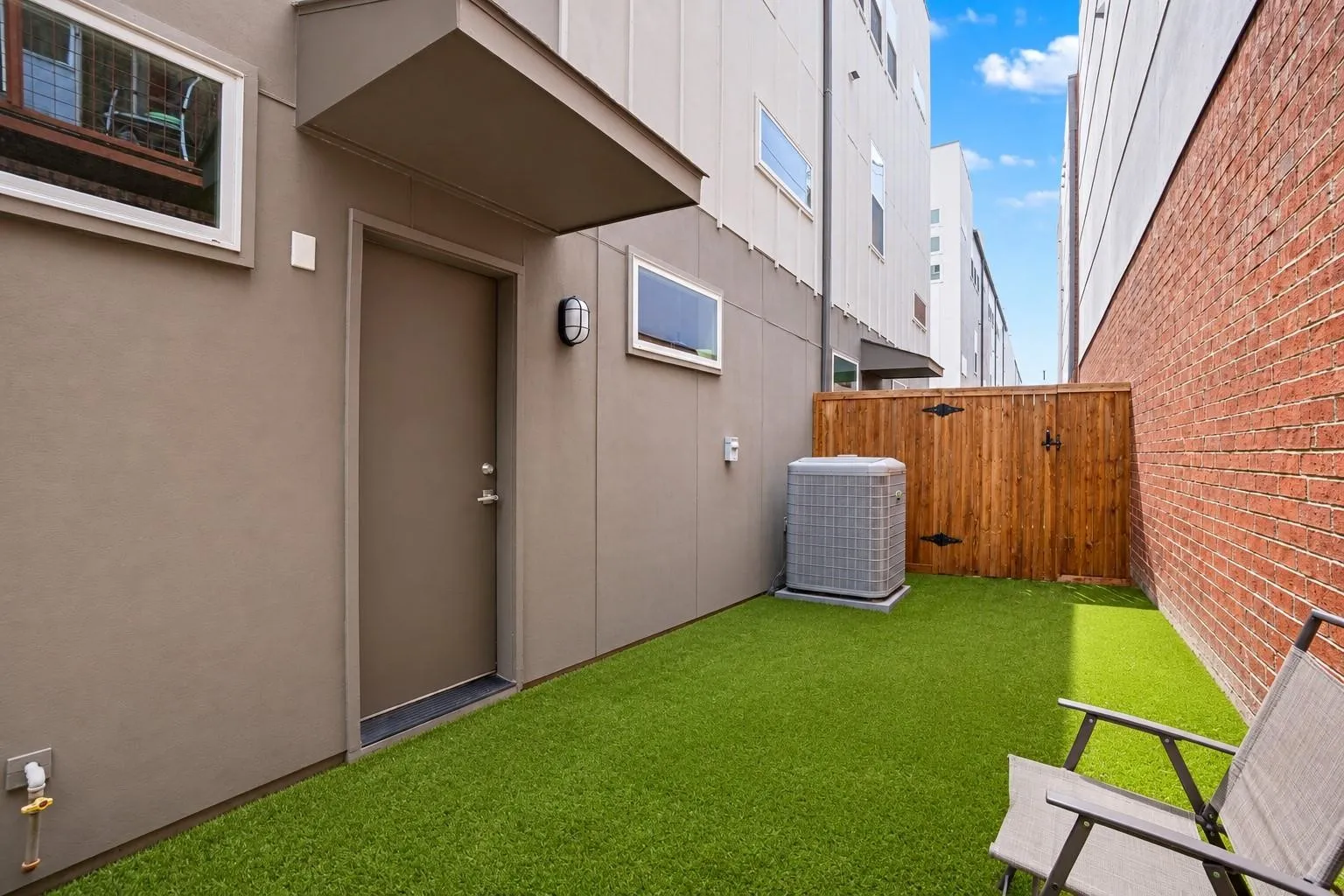 Private outdoor space featuring artificial turf, a wood fence, and a brick wall