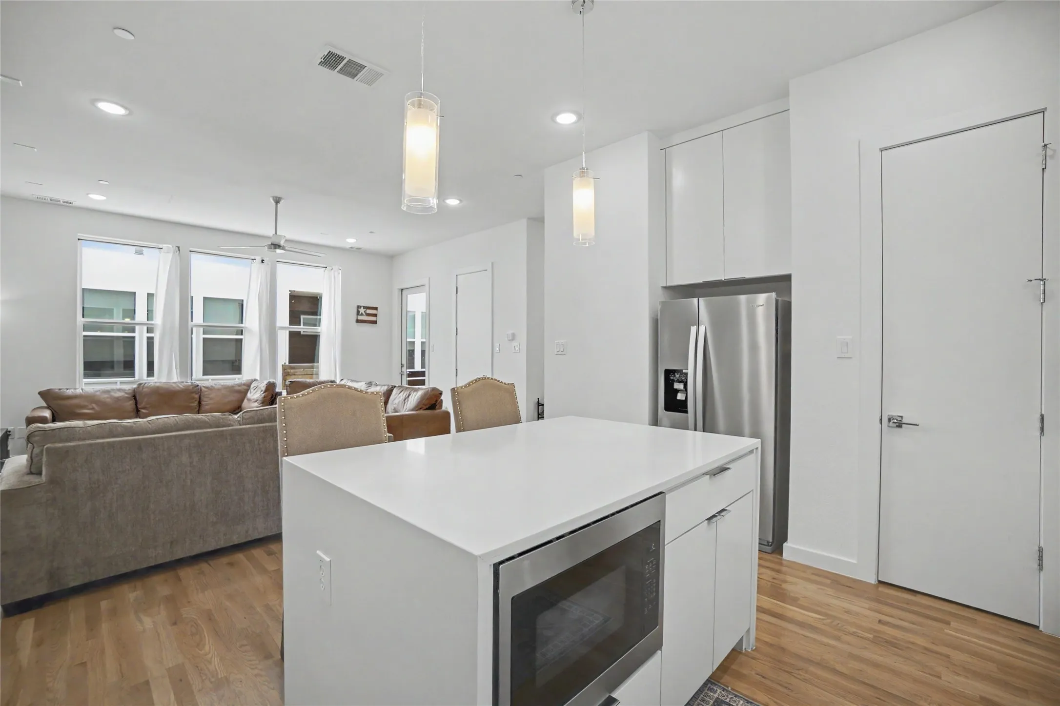 Open-concept living space featuring wood-finish flooring, recessed lighting, and a kitchen island with integrated microwave