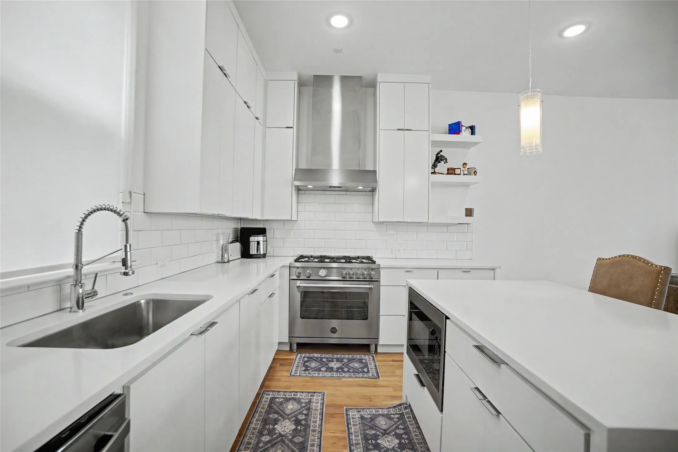White cabinetry with modern hardware, stainless steel appliances, undermount sink with a gooseneck faucet, subway tile backsplash, and light-toned countertops