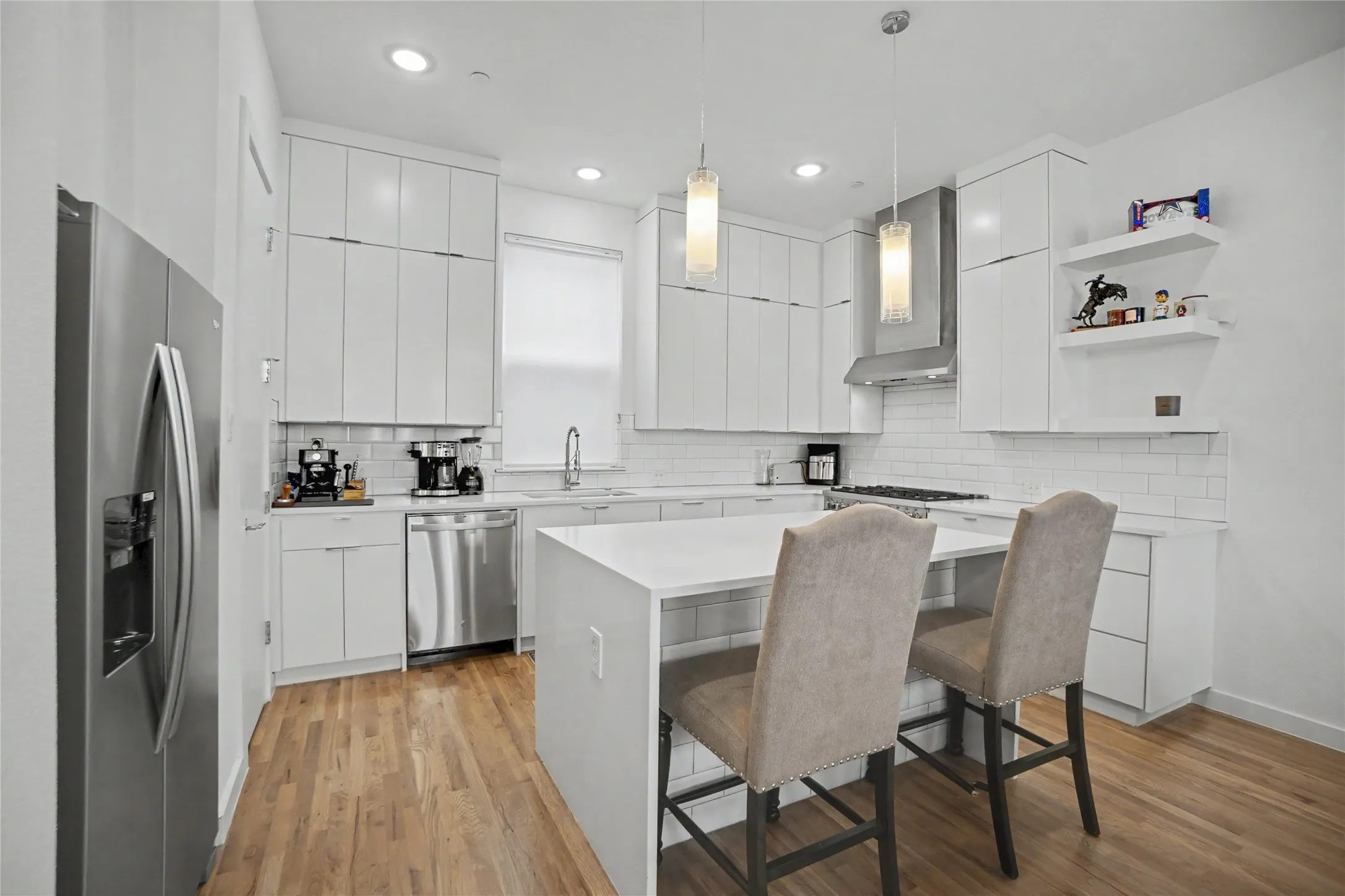 Modern kitchen featuring wood-finish flooring, white cabinetry, integrated stainless steel appliances, a white subway tile backsplash, and a central island with a solid surface countertop