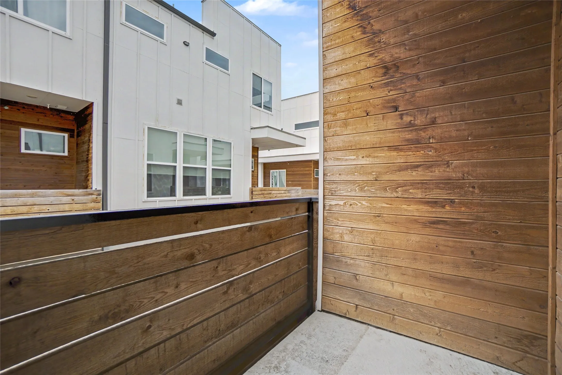Private patio with wood-finish horizontal plank fencing, concrete flooring, and a modern exterior featuring white siding and wood-finish accents
