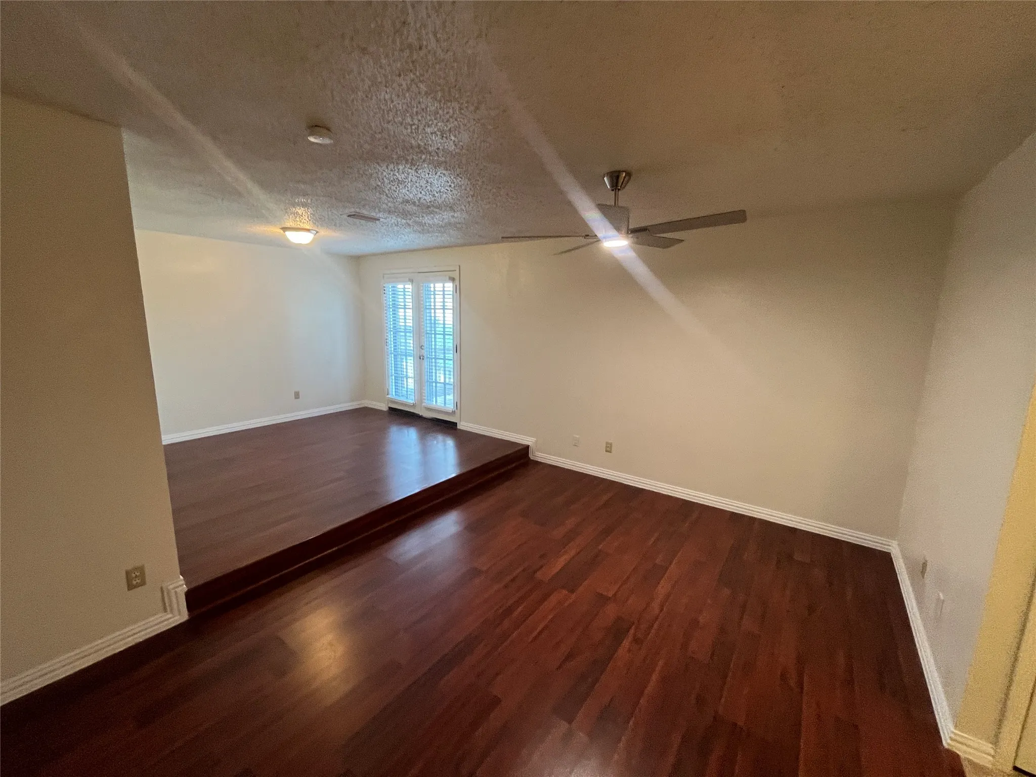 Hardwood flooring throughout, two-tier room design, ceiling fan, and French doors