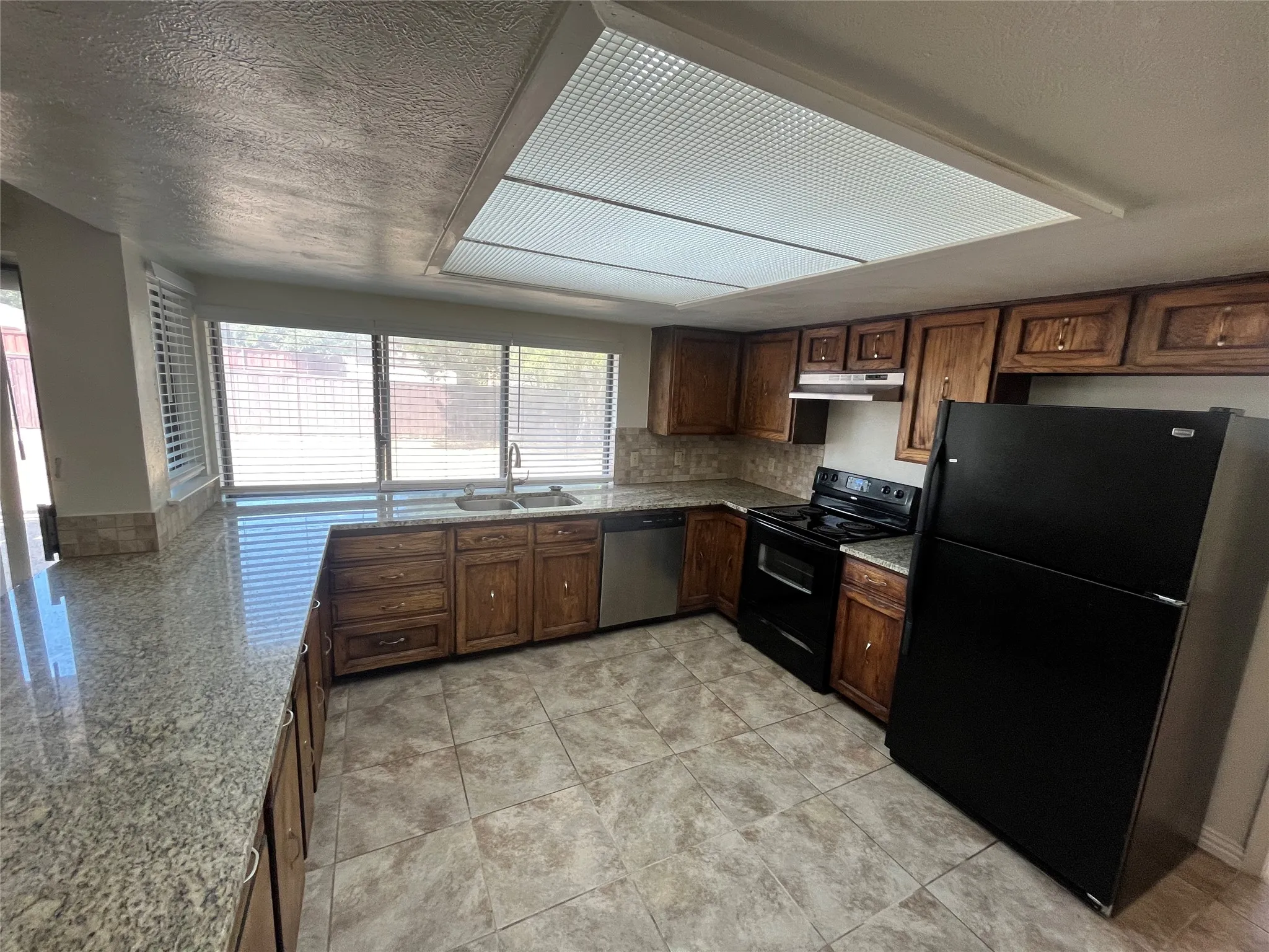 Kitchen featuring ample wood cabinetry, a double basin sink, black appliances, and durable tile flooring
