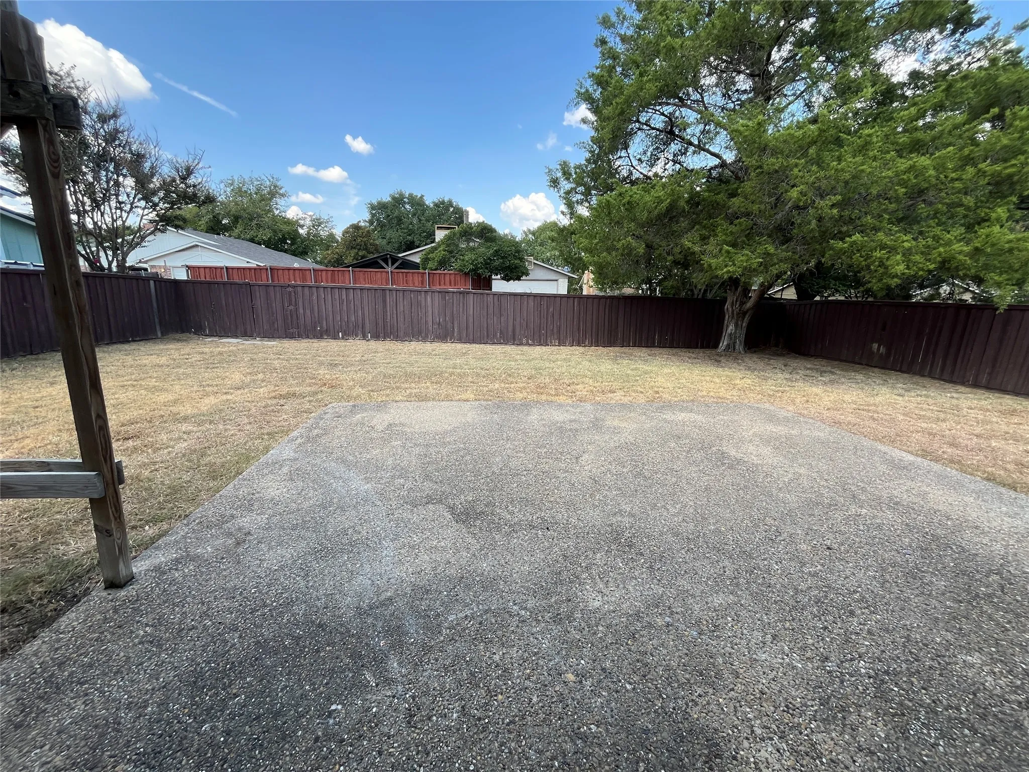 Expansive outdoor space featuring a large concrete patio, a tall privacy fence, and mature trees