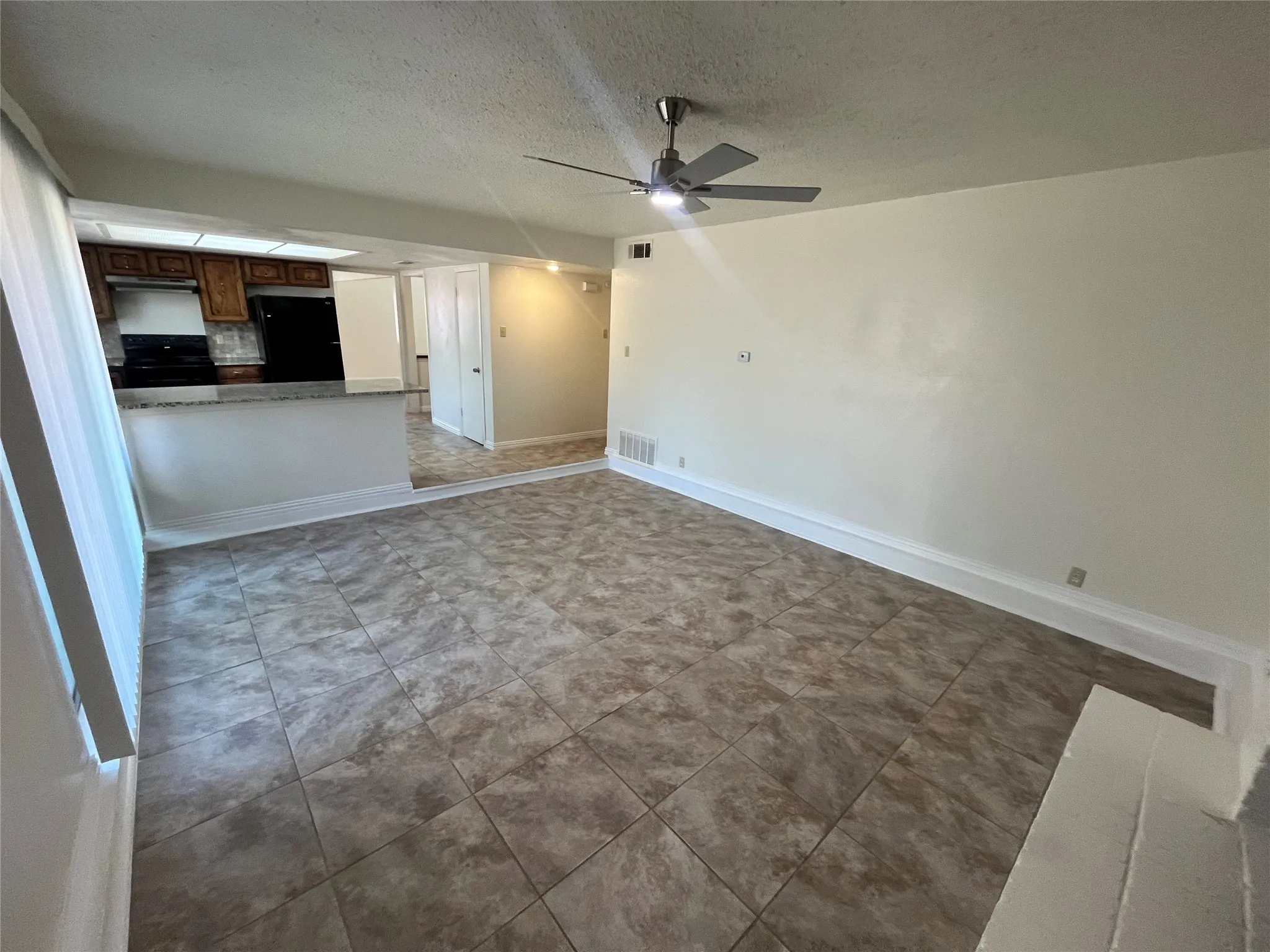 Spacious living area featuring large format tile flooring, a contemporary ceiling fan, and a partial wall separating the kitchen with a breakfast bar