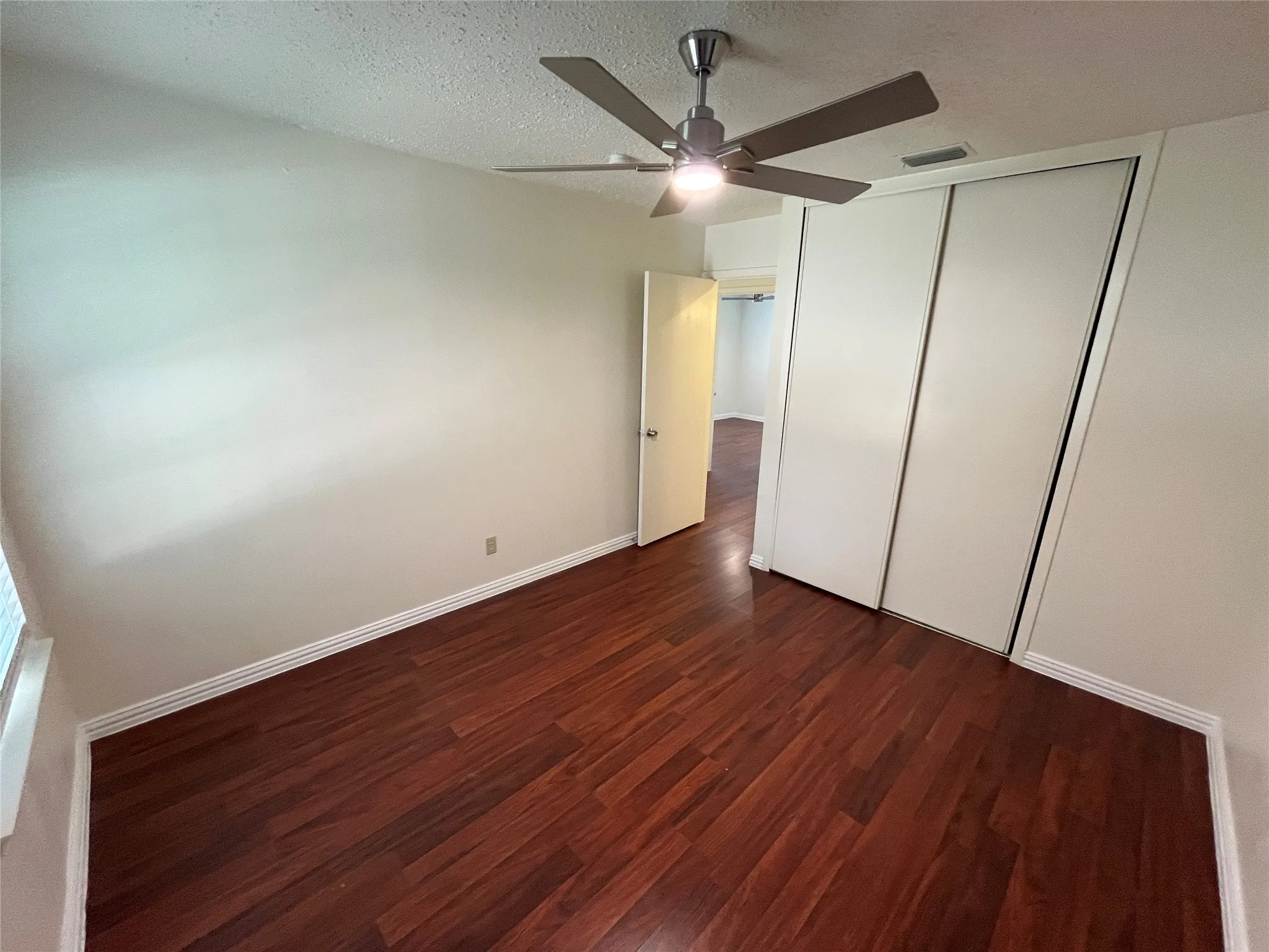Wood-finish flooring, sliding closet doors, ceiling fan with integrated lighting, and neutral wall paint