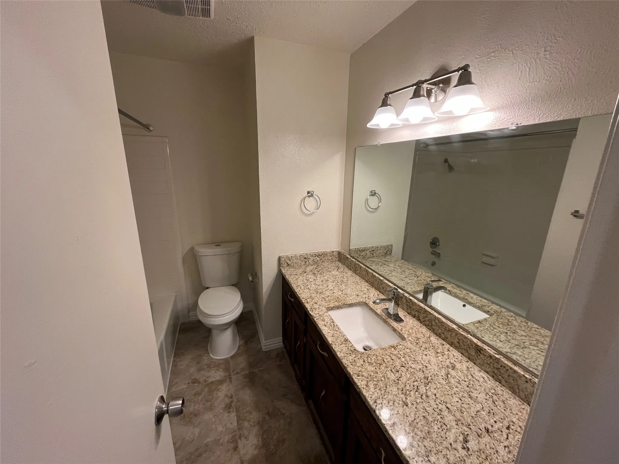 Bathroom featuring a vanity with a light-toned speckled countertop, dark wood-finish cabinetry, an undermount sink, and a large wall-mounted mirror