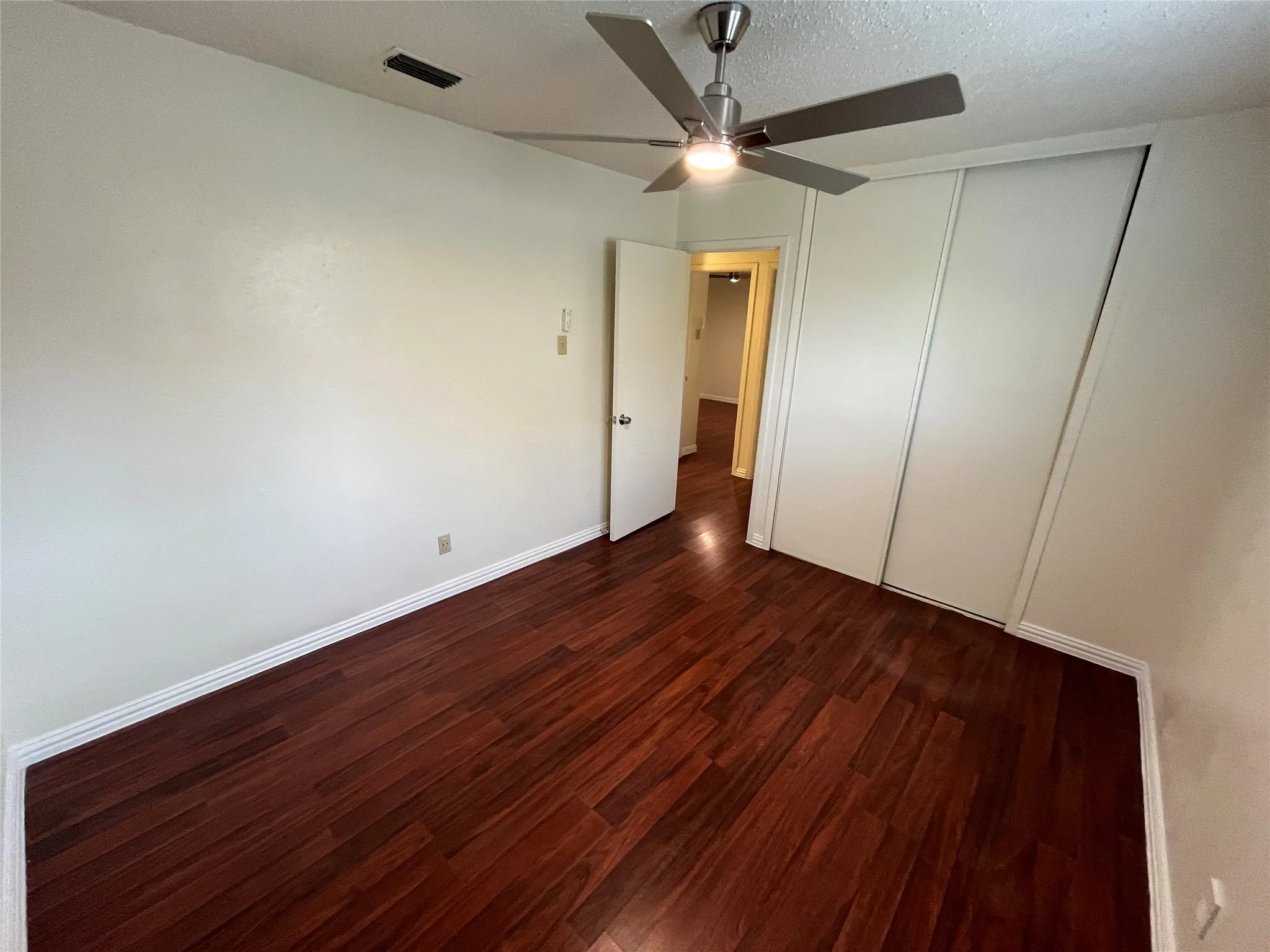 Rich wood-finish flooring, bright white walls, modern ceiling fan with lighting, and white sliding closet doors