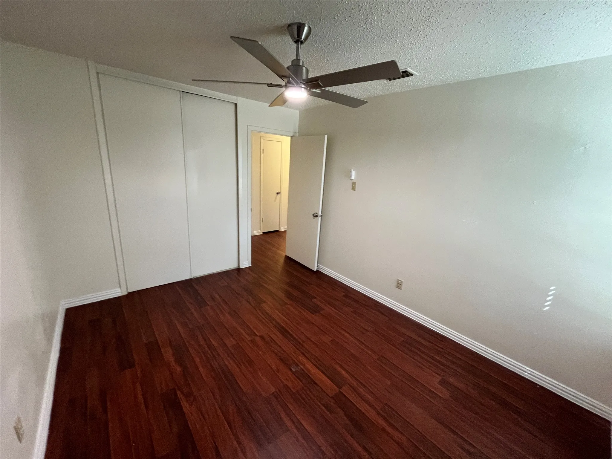 Dark wood-finish flooring, white walls, and a ceiling-mounted fan with integrated lighting