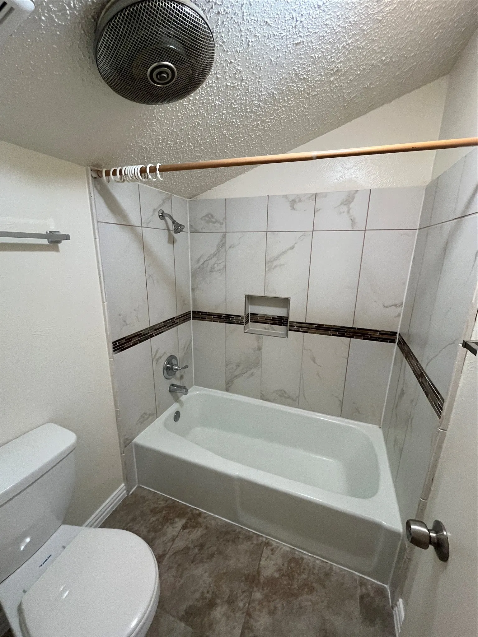 White bathtub with a built-in shower niche, surrounded by marble-patterned wall tiles and a decorative accent band