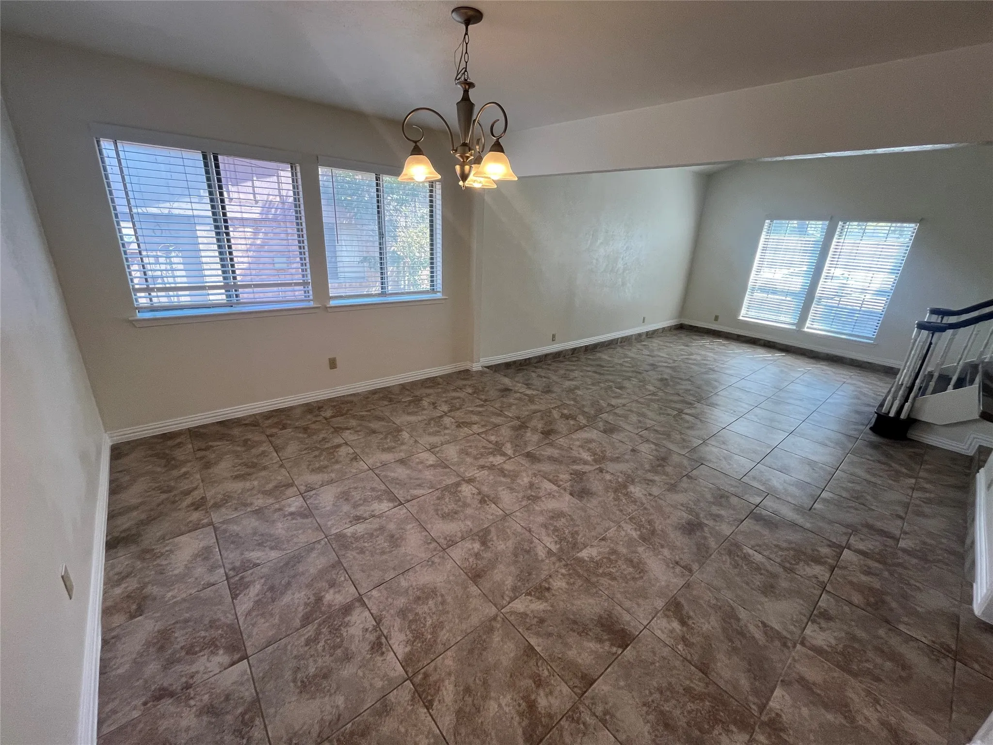Spacious room featuring tile flooring, multiple windows, a chandelier light fixture, and a stairway with a railing