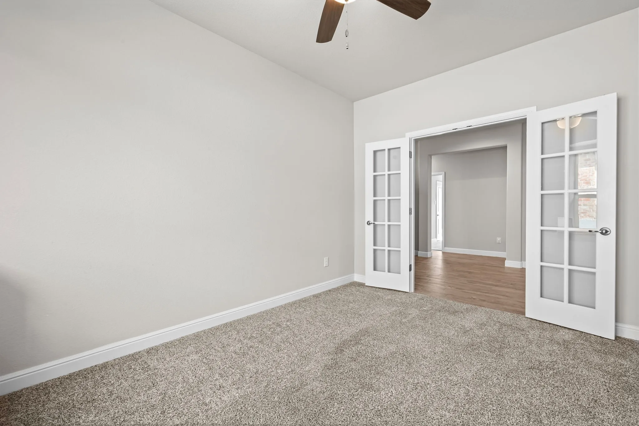 French doors with glass panels, carpet flooring, ceiling fan with light fixture, light gray wall paint, and wood-finish flooring in the adjacent room