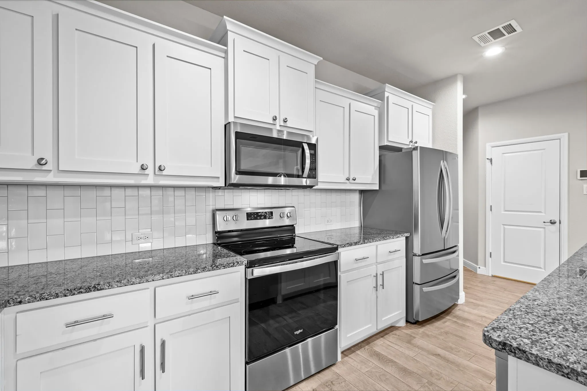 White shaker cabinetry, stainless steel appliances, granite countertops, subway tile backsplash, and wood-finish flooring