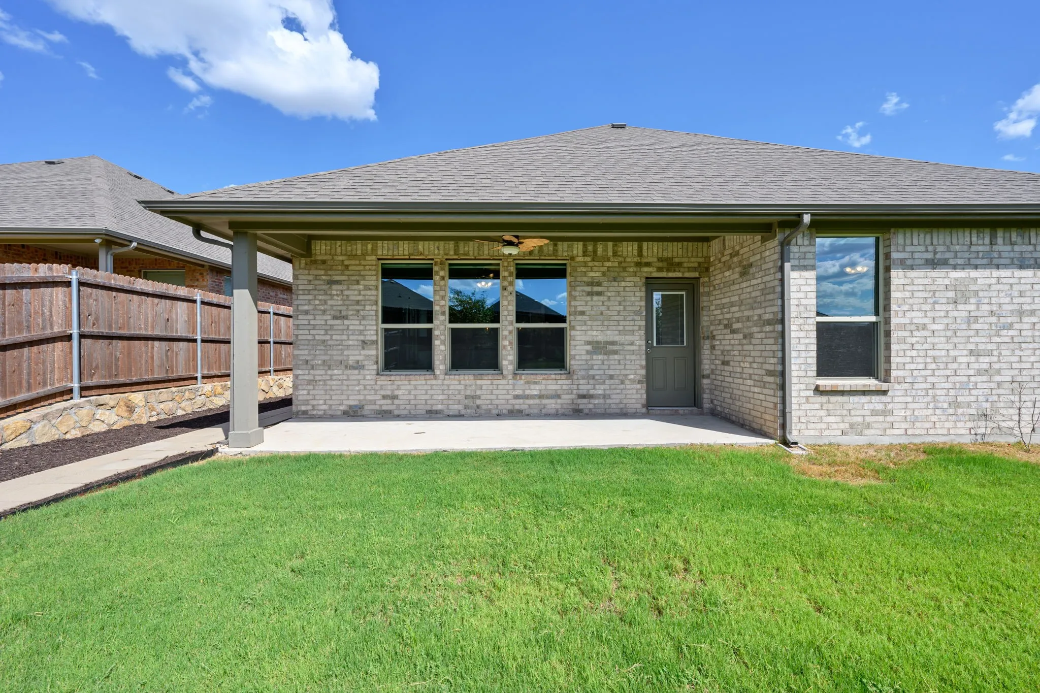 Rear exterior featuring a covered patio, brick facade, and a fenced yard with a stone retaining wall