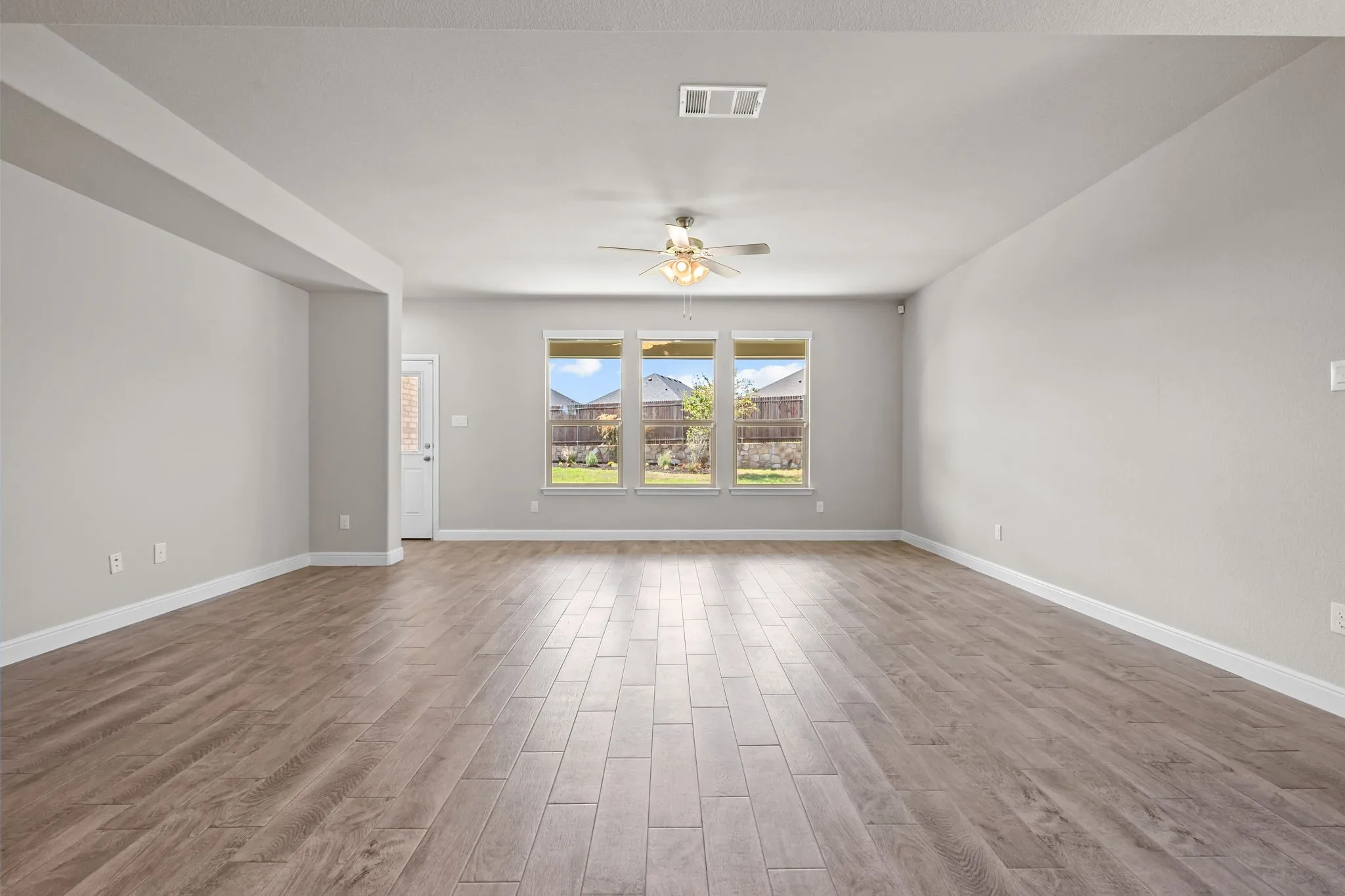 Spacious room featuring wood-finish flooring, light gray walls, and a ceiling fan