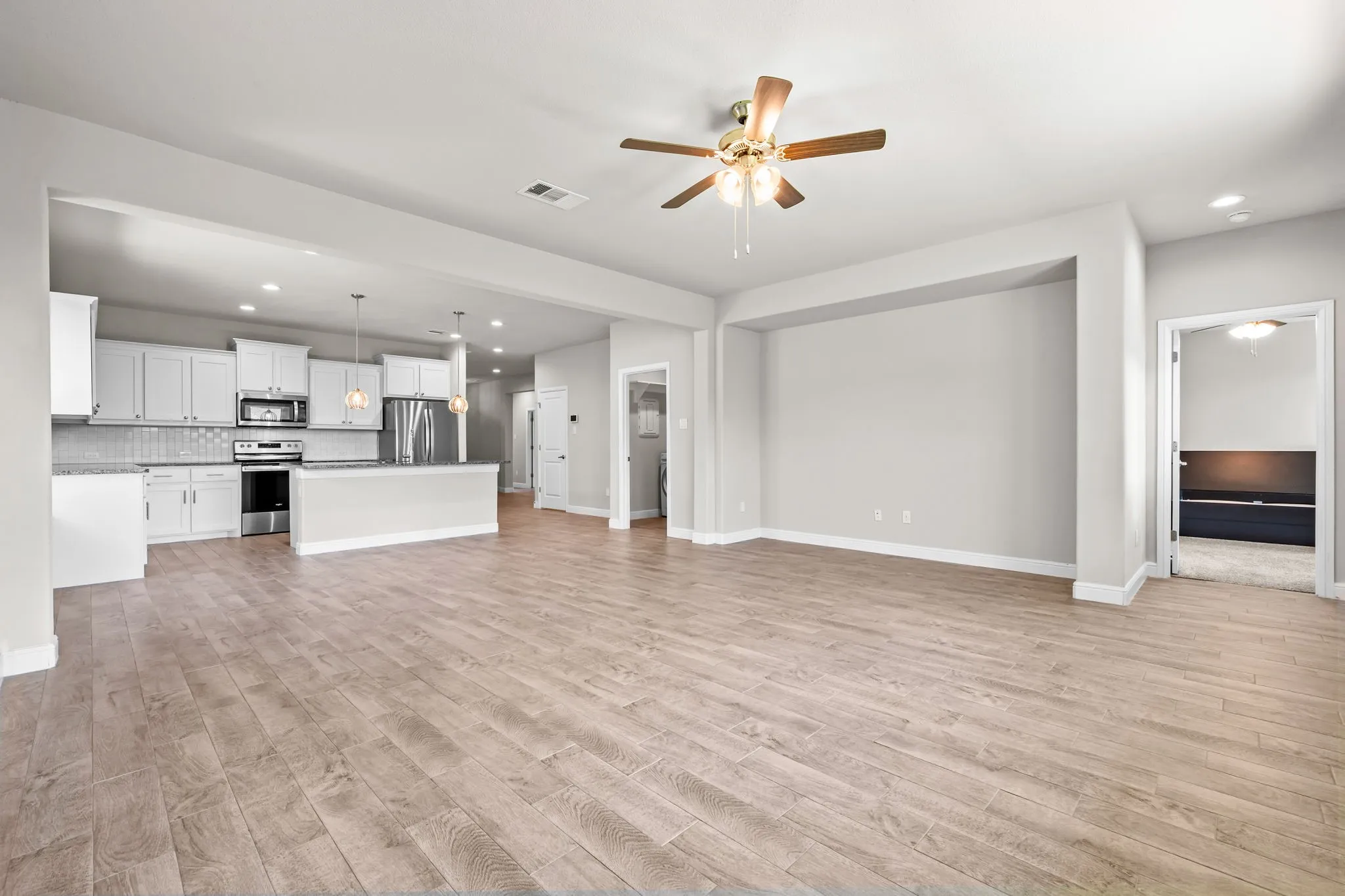 Open-concept living space featuring wood-finish flooring, a kitchen with white cabinetry, stainless steel appliances, and a breakfast bar