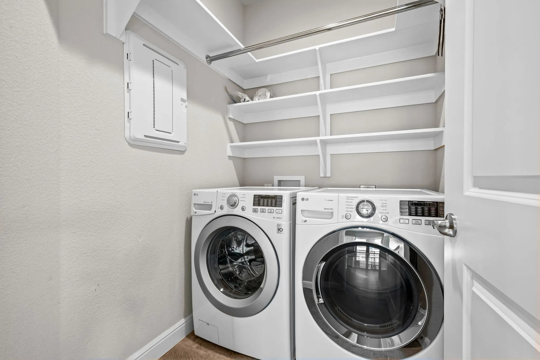 Dedicated laundry area featuring front-loading appliances, white shelving, and a hanging rod