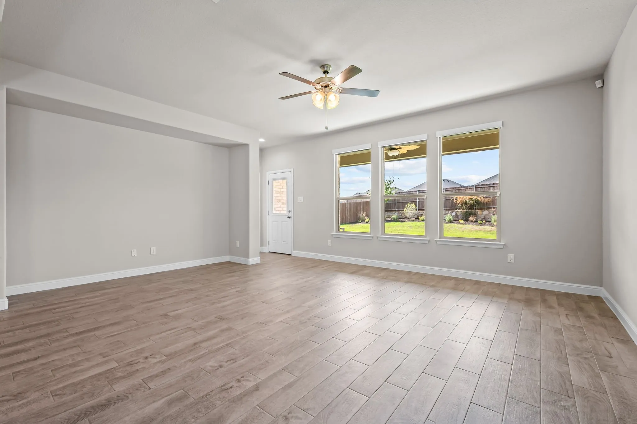 Expansive living area with wood-finish flooring, three large windows, and a ceiling fan