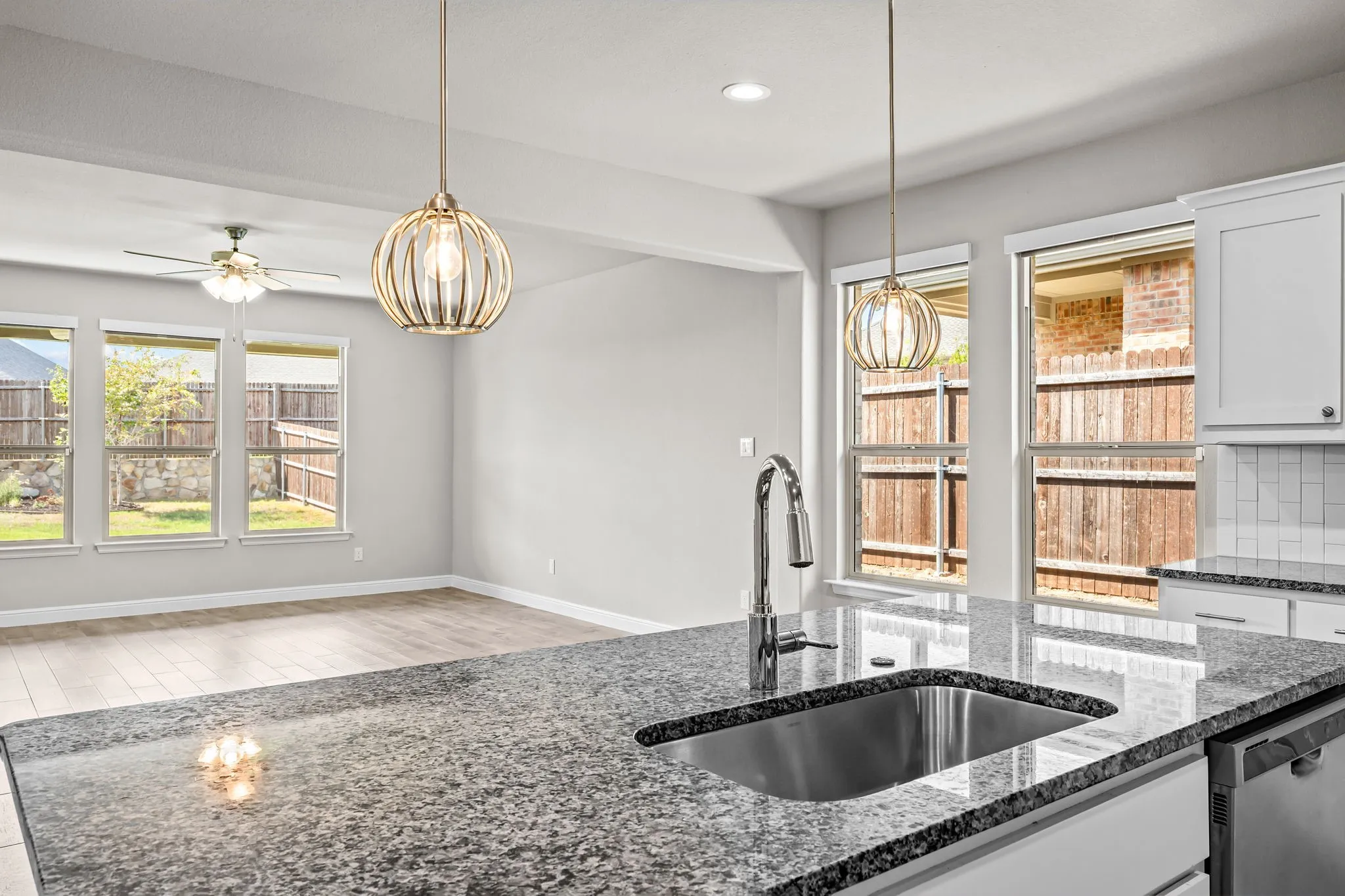 Expansive granite countertops, stainless steel sink with a gooseneck faucet, white shaker-style cabinetry, and wood-finish flooring