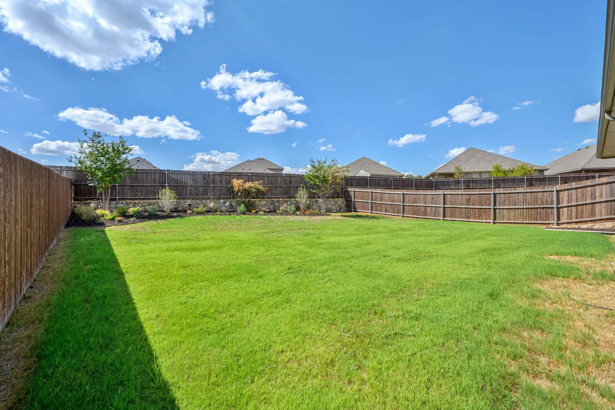 Expansive backyard featuring a manicured lawn, wood fencing, and mature landscaping