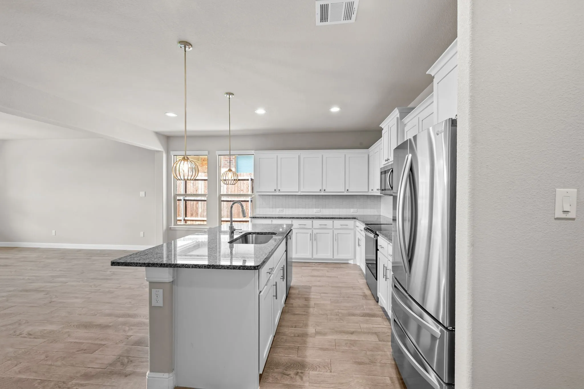 Kitchen featuring a granite-topped island, stainless steel appliances, white cabinetry, tile backsplash, and wood-finish flooring