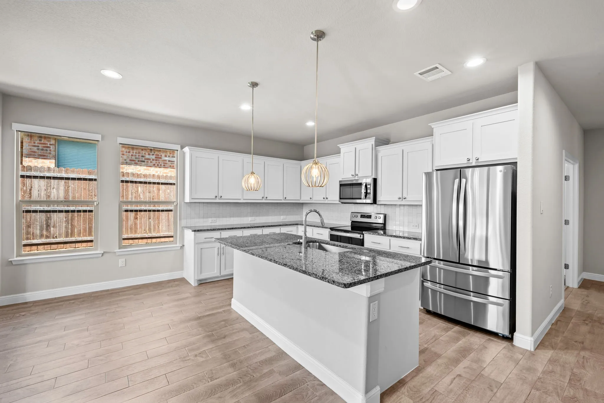 Kitchen featuring an island with stone countertops, white shaker cabinetry, stainless steel appliances, and wood-finish flooring