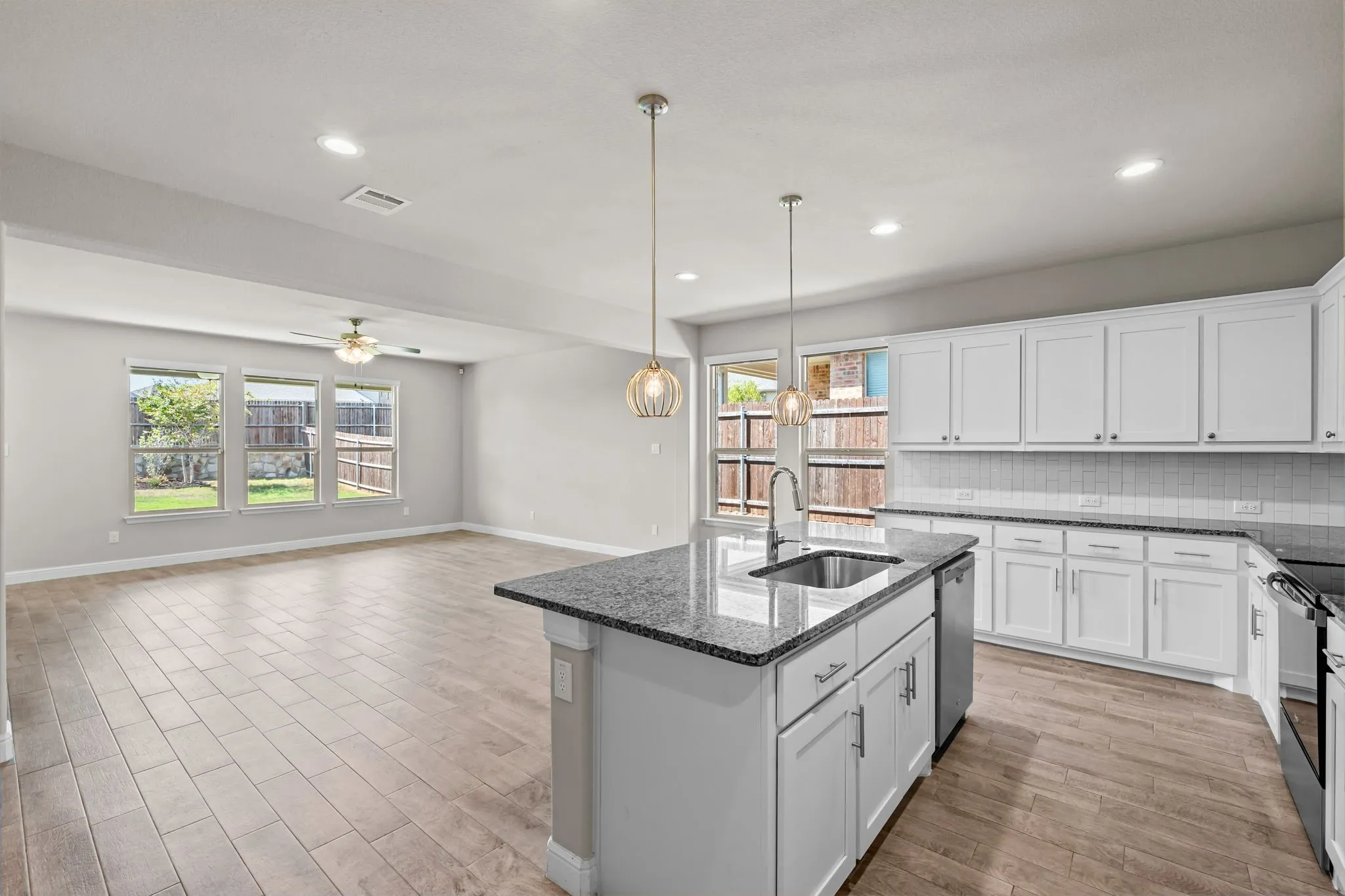 Spacious open-concept living area featuring wood-finish flooring, white cabinetry, and granite countertops