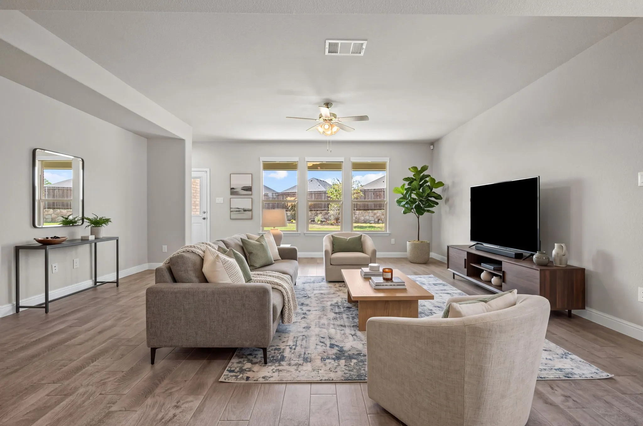 Spacious living area featuring wood-finish flooring, ample natural light from multiple windows, and a ceiling fan