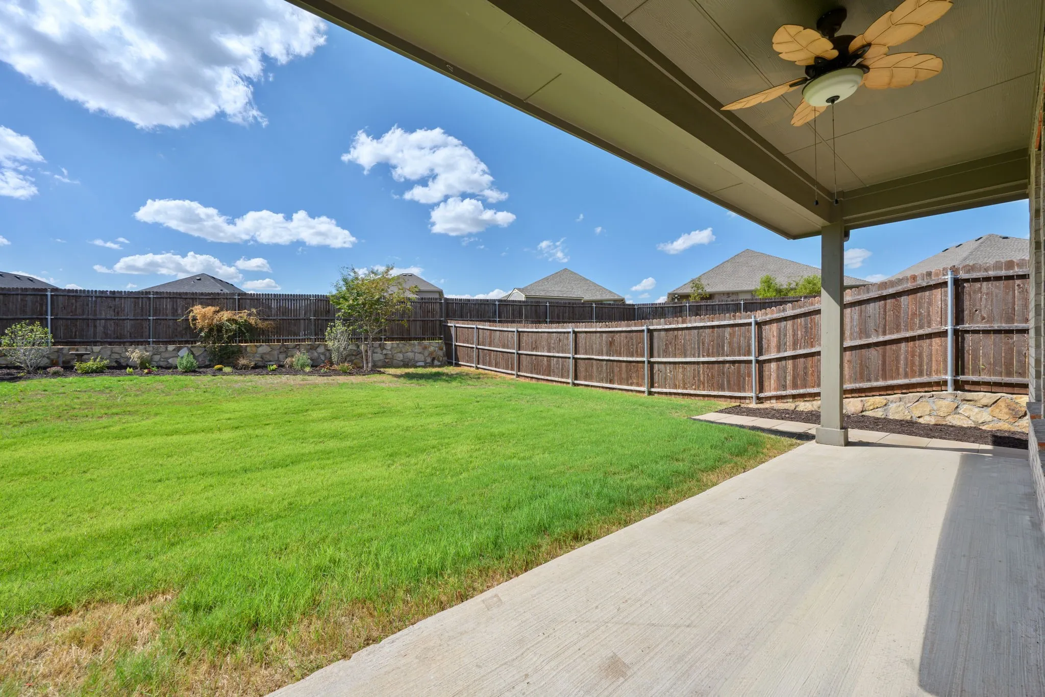 Covered patio with an outdoor ceiling fan, concrete flooring, and a stone retaining wall