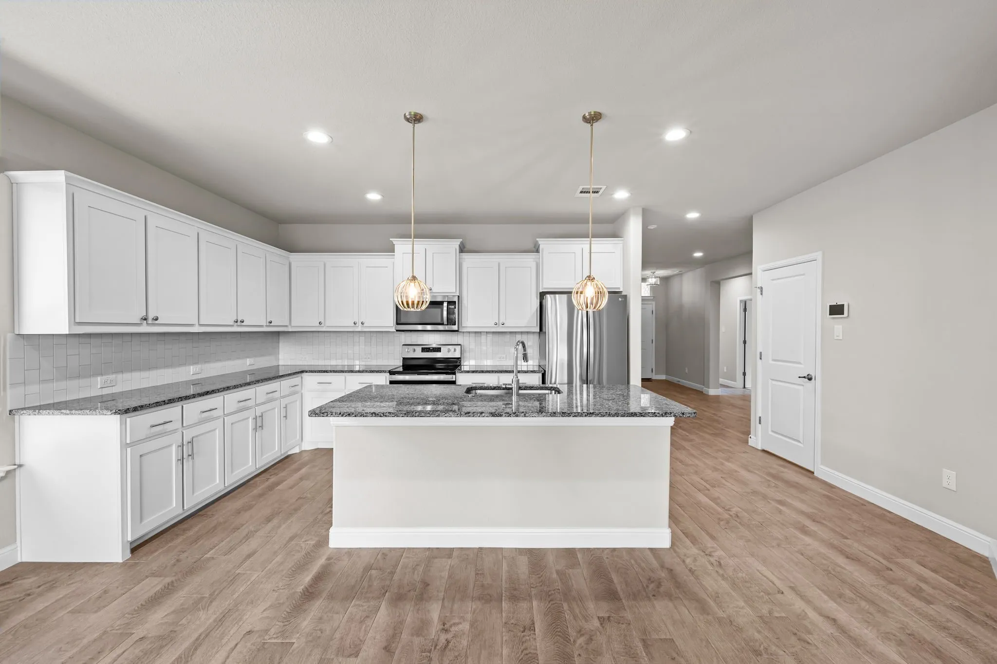 Spacious kitchen featuring white shaker cabinetry, stone countertops, a large island with sink, and wood-finish flooring