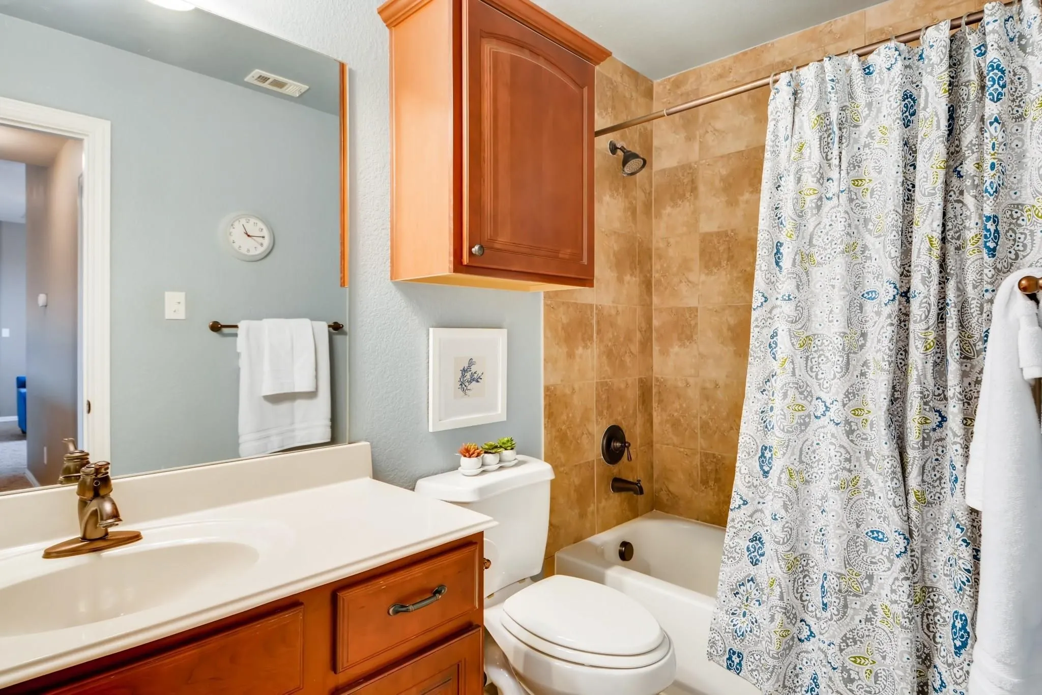 Bathroom featuring a vanity with a white countertop and wood-finish cabinetry, a built-in shower-over-tub, and warm-toned tiled shower surround