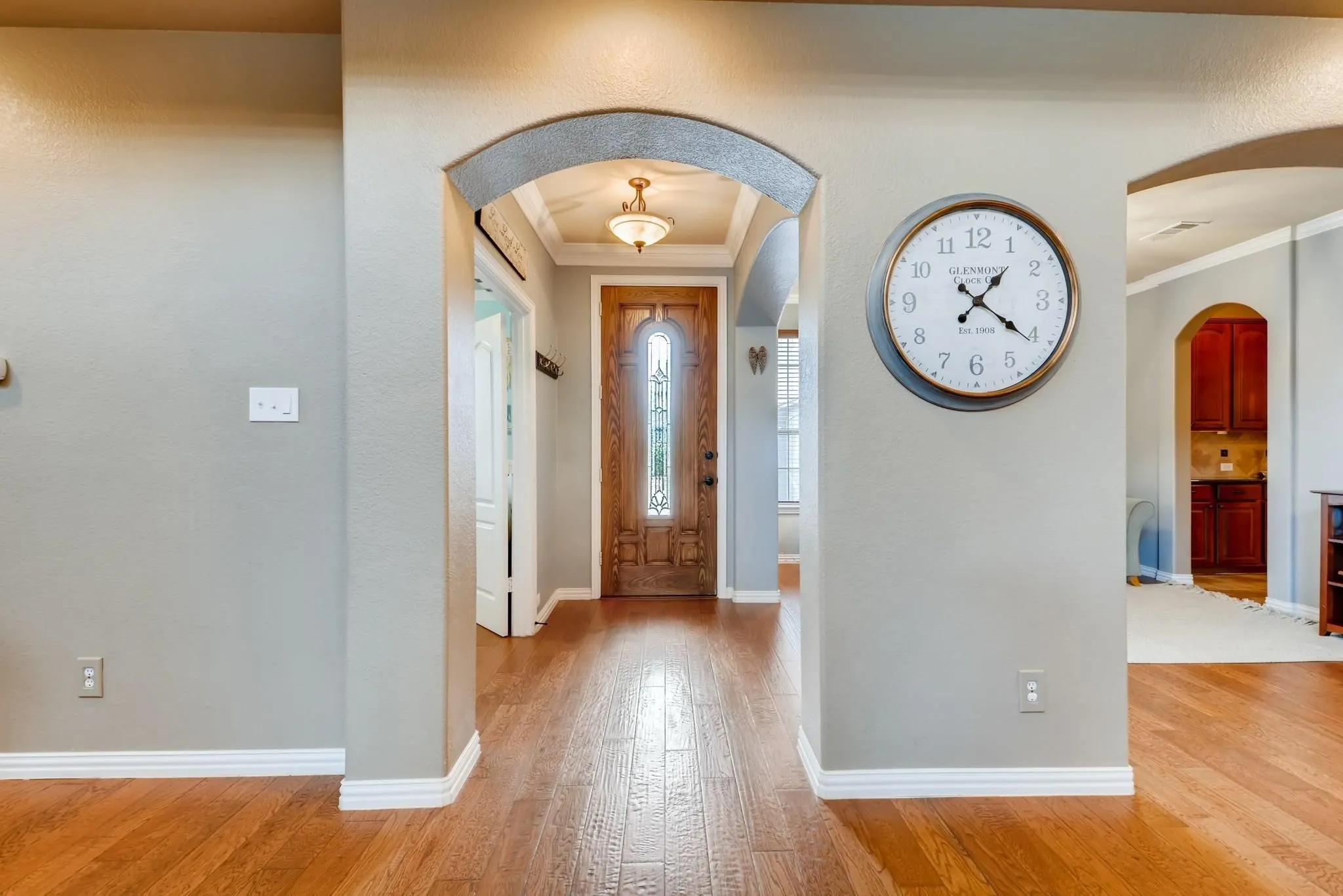 Wood-finish flooring throughout, arched doorways, and a paneled front door with decorative glass