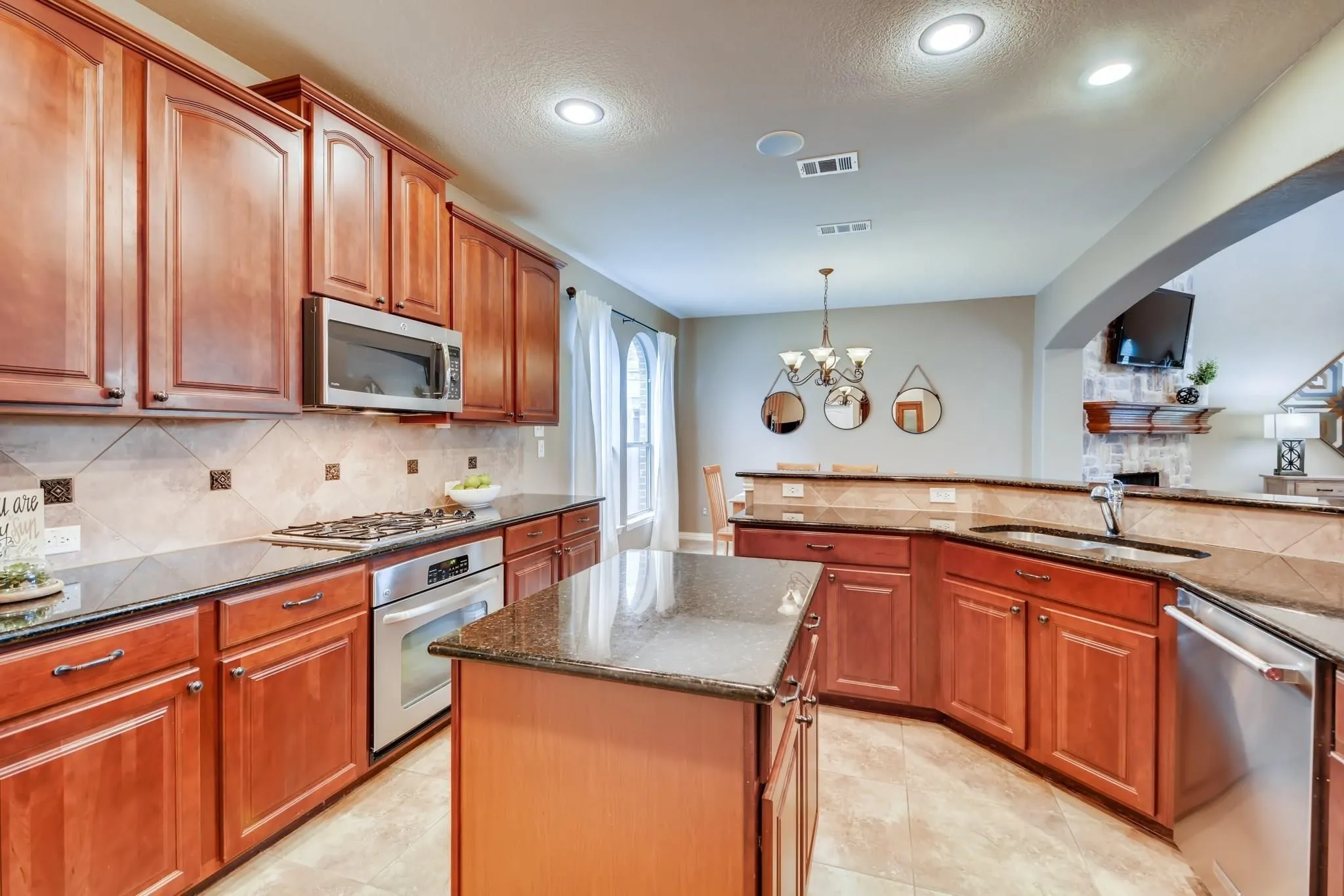 Cherry wood cabinetry, stainless steel appliances, stone countertops, tile backsplash, and recessed lighting