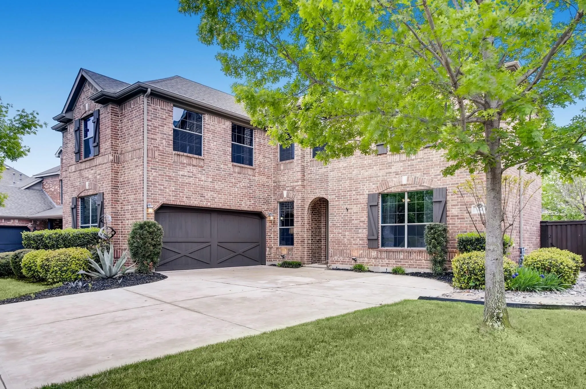 Brick exterior, two-story structure, dark-stained garage doors, arched entry, and established landscaping