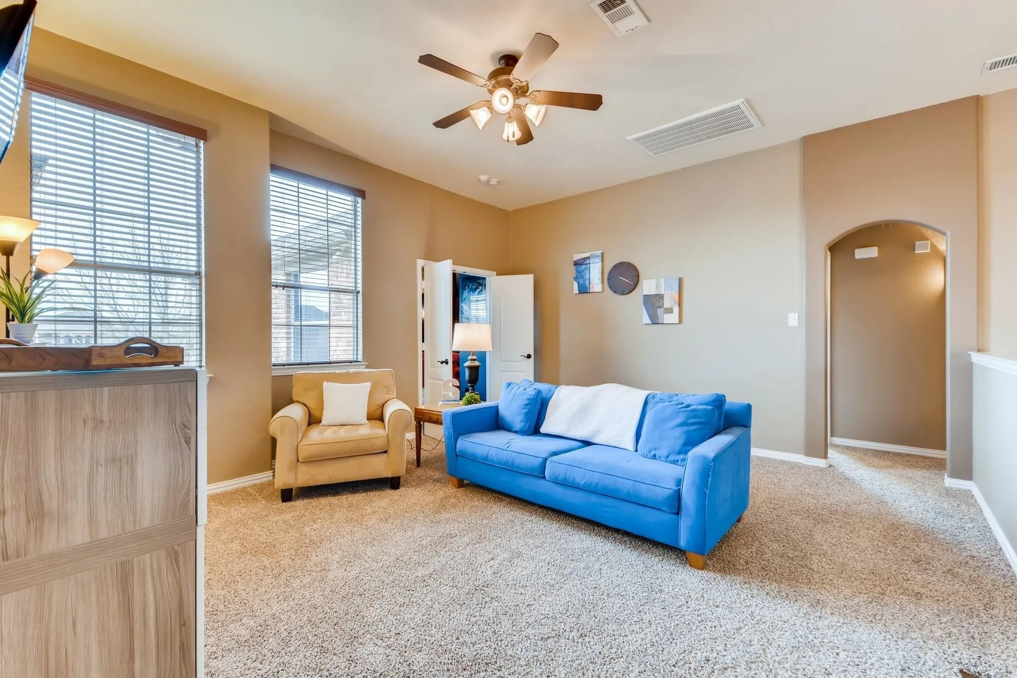 Carpeted room featuring multiple windows with blinds, a ceiling fan with integrated lighting, and an arched doorway