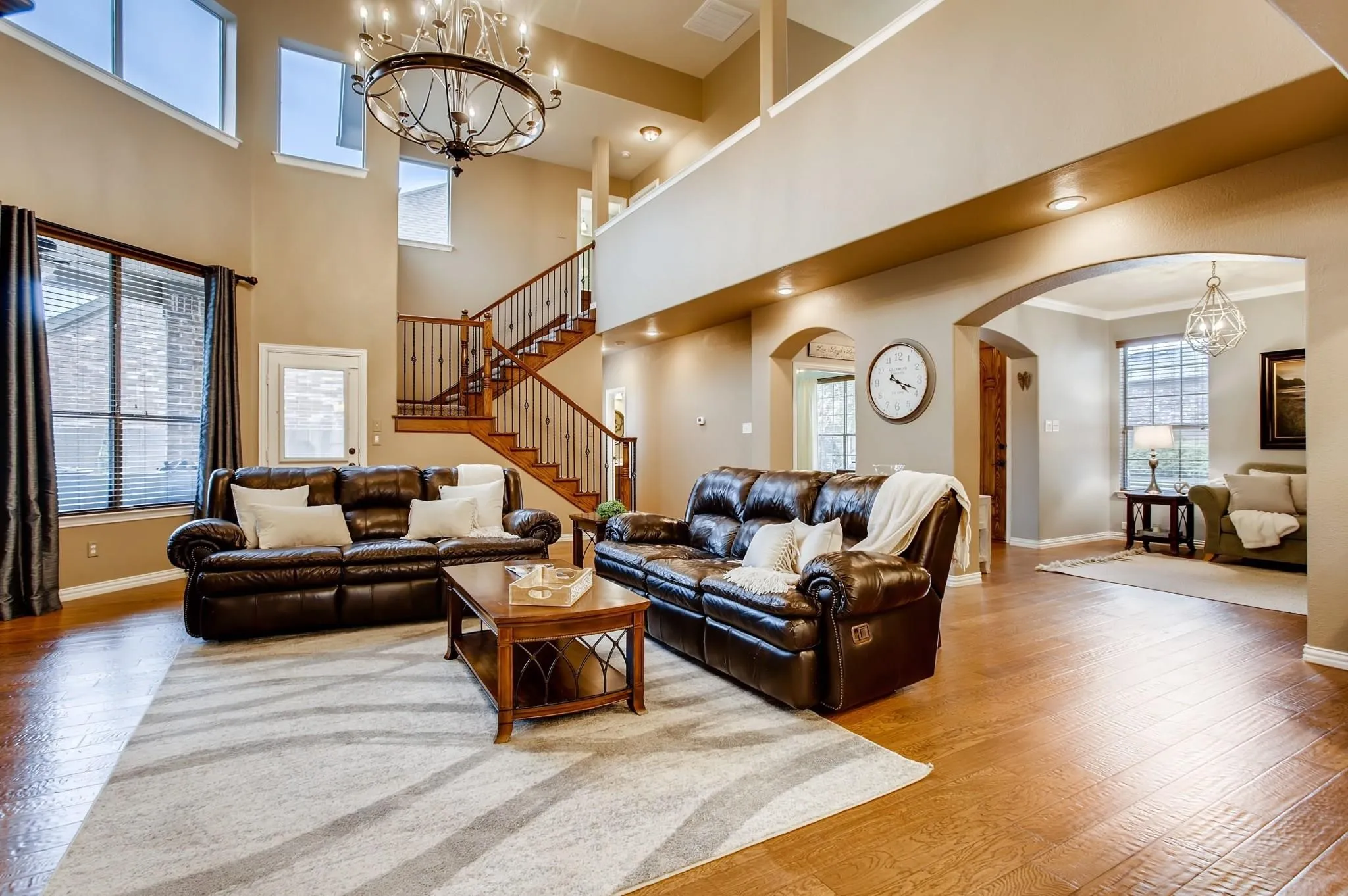 High ceilings with a decorative chandelier, wood-finish flooring, a grand staircase with wrought iron balusters, and multiple arched doorways