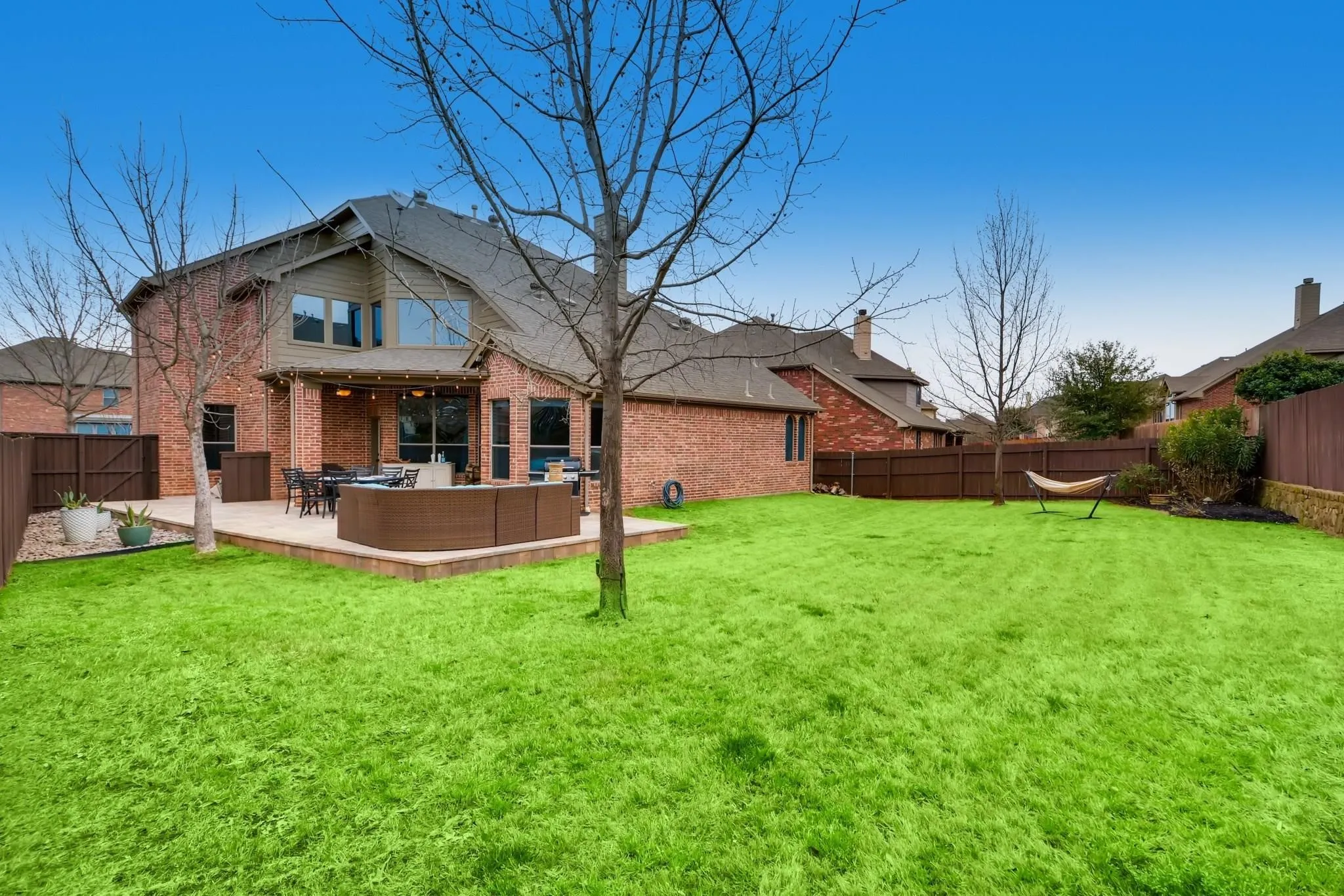Spacious backyard featuring a large patio, brick exterior, and wood fencing