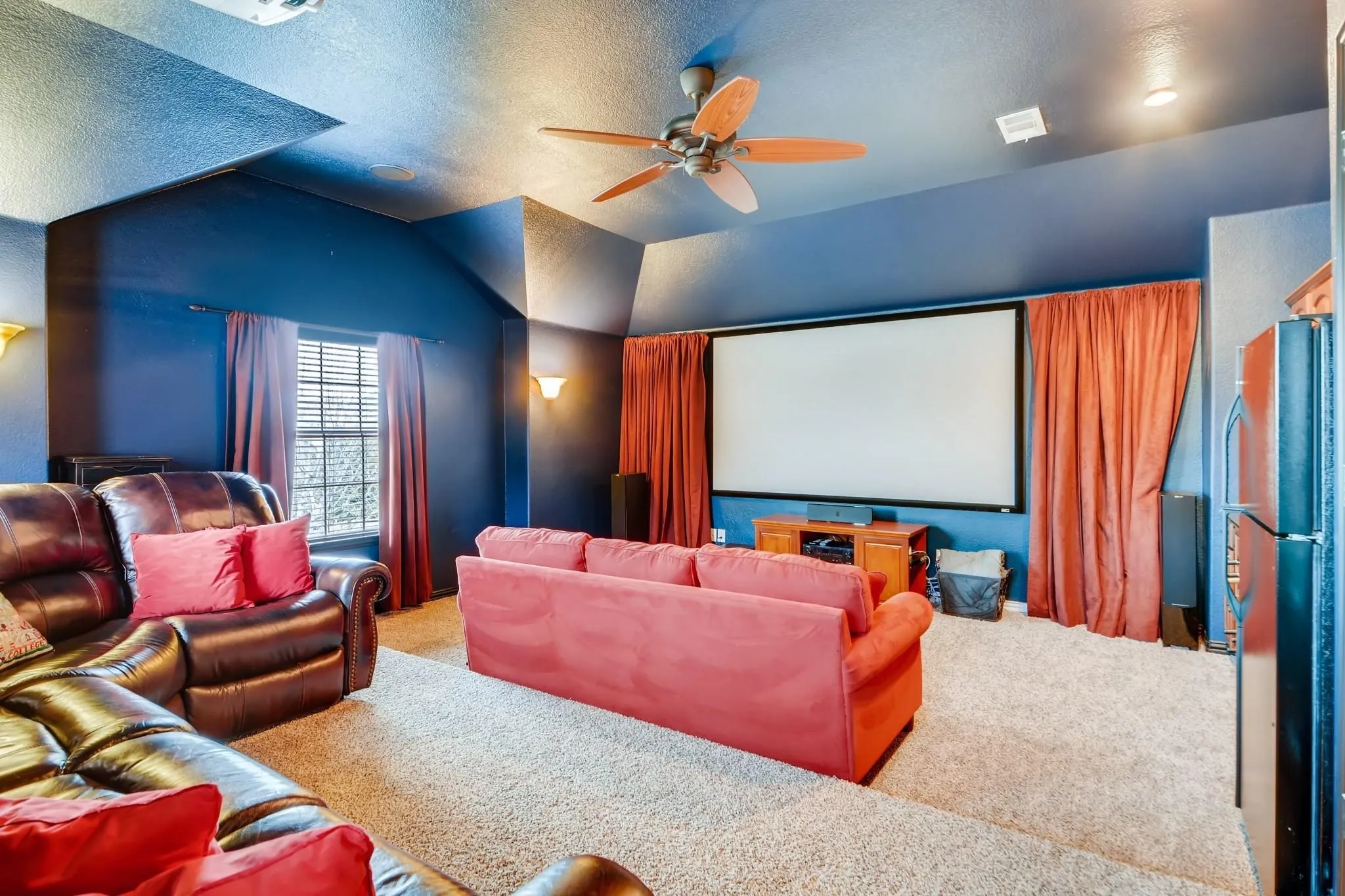 Media room featuring a projection screen, built-in cabinetry, ceiling fan, and sconce lighting