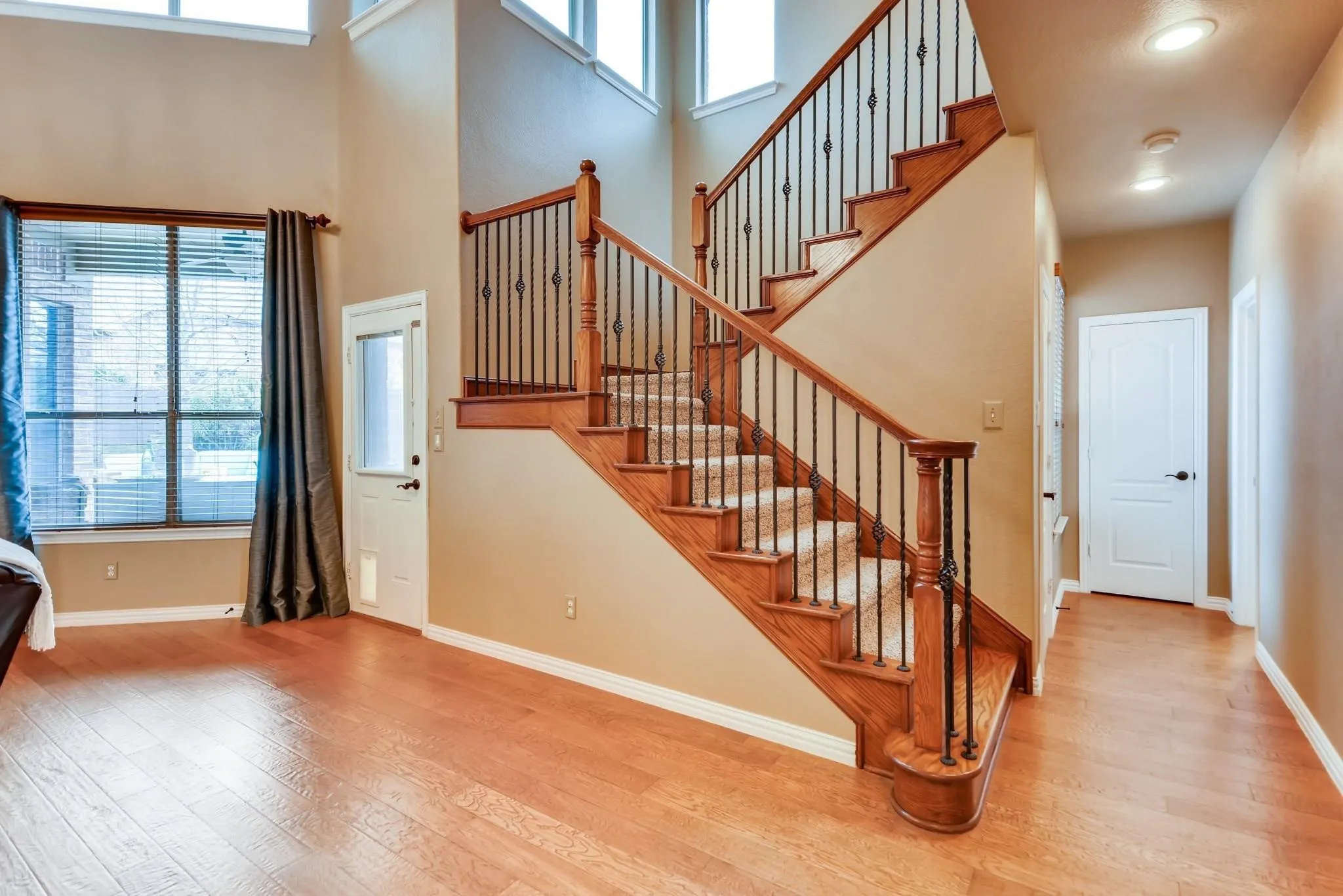Wood-finish flooring throughout, featuring a staircase with carpeted treads and wrought iron balusters