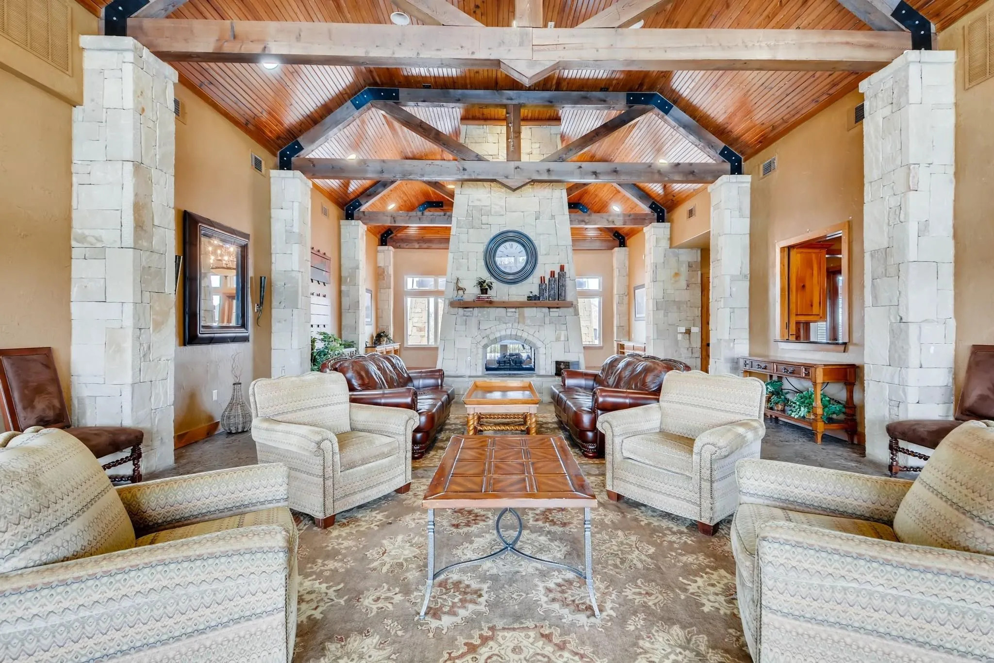 Vaulted wood-paneled ceiling with exposed beams, stone fireplace, stone pillars, and wood-finish flooring