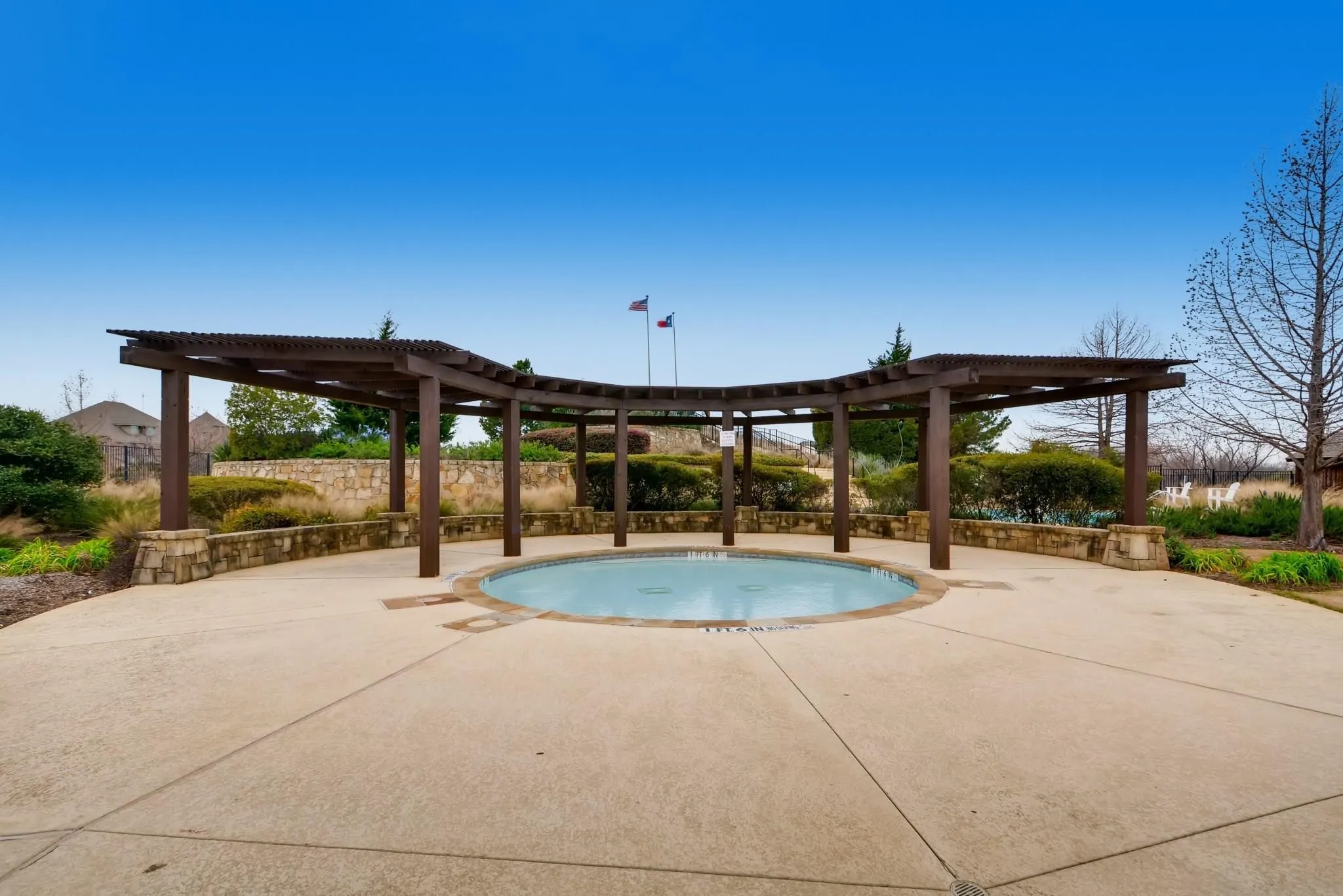 Circular water feature with surrounding concrete decking, shaded by an expansive wooden pergola structure